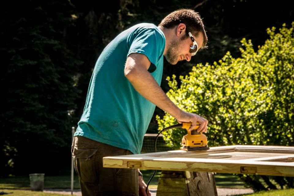 man with sunglasses on sanding a door