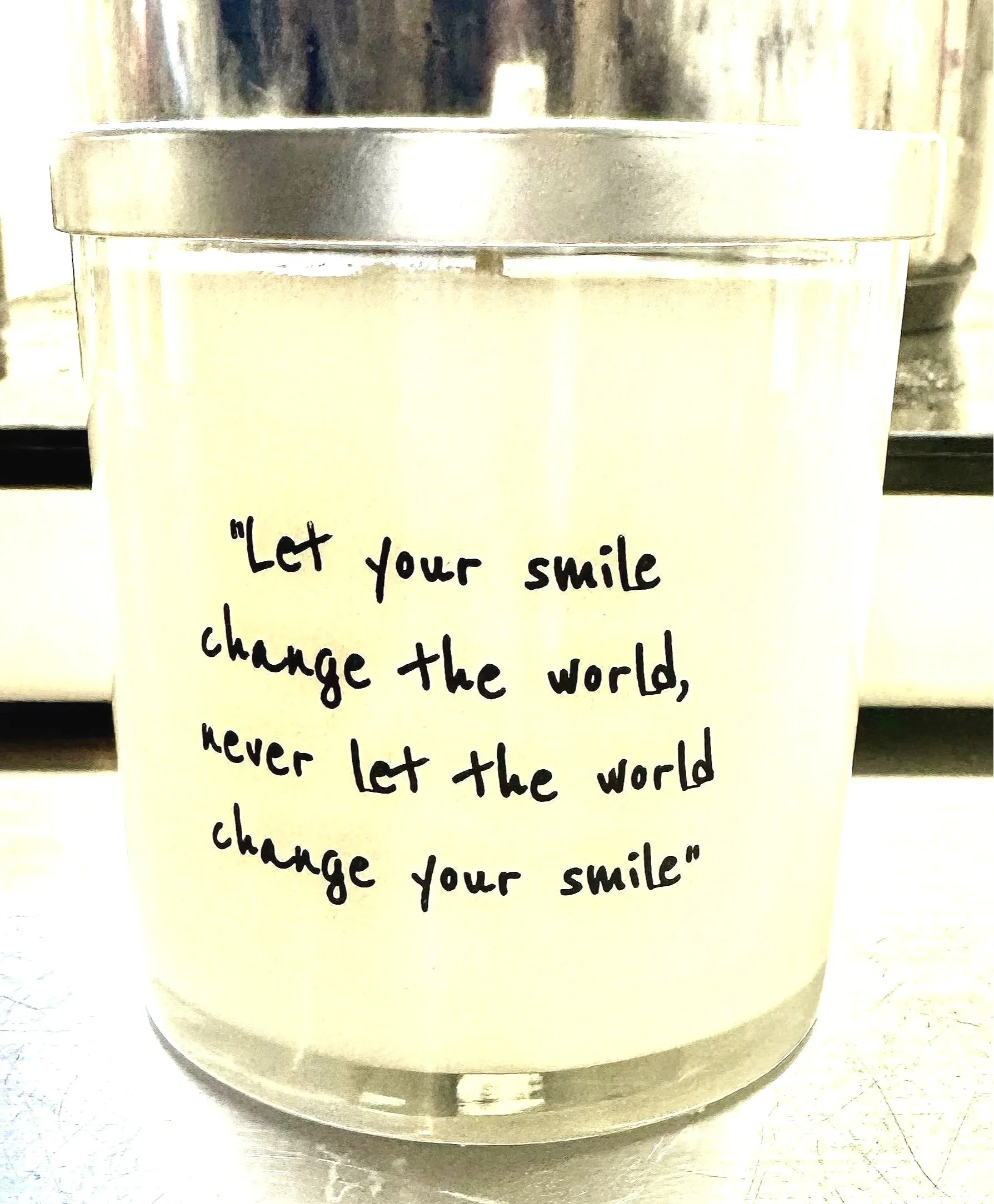 A cream-colored candle with a motivational quote written on it: "Let your smile change the world, never let the world change your smile."