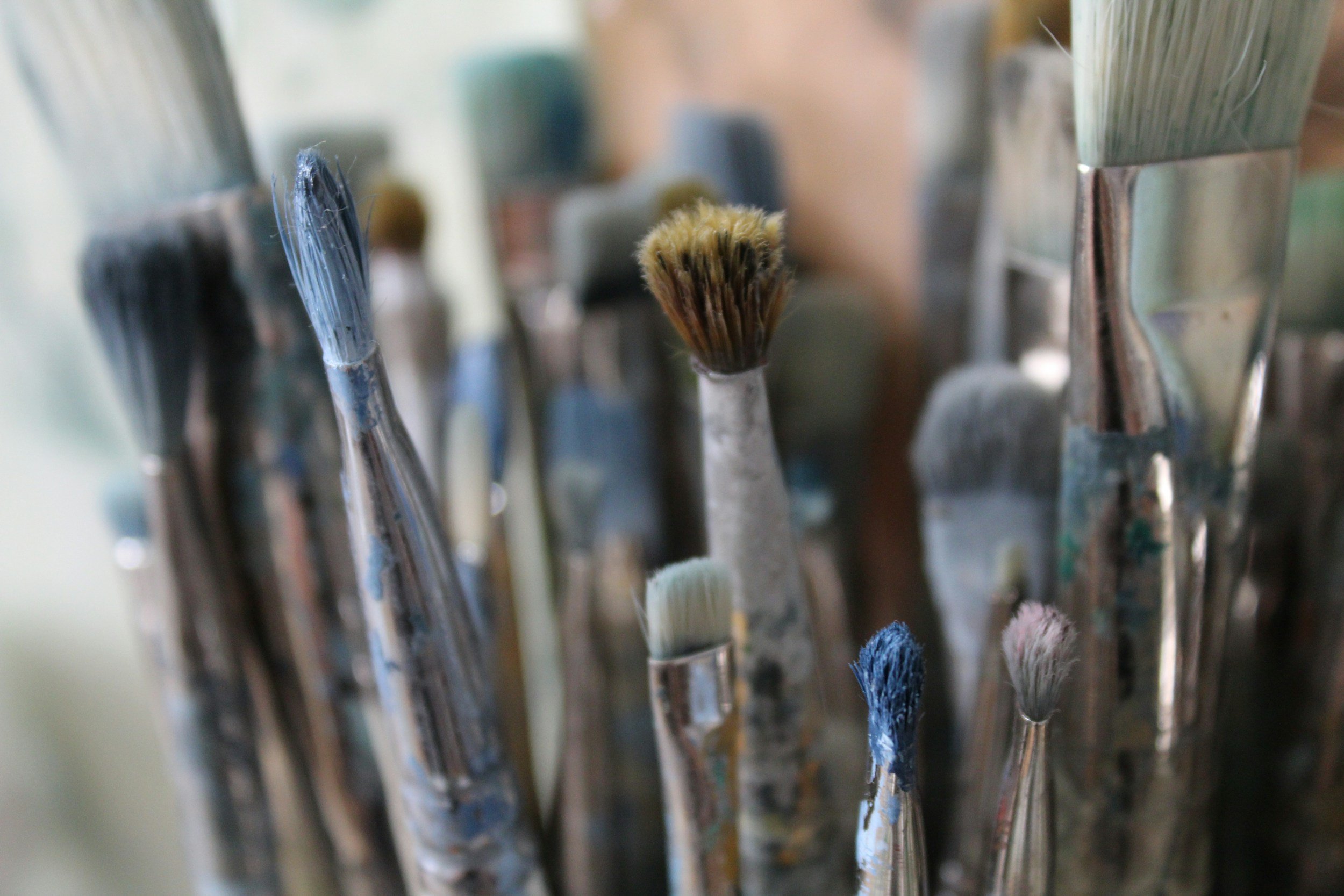 Assorted paintbrushes with varying bristle types and colors, including blue and white, standing upright in a container.