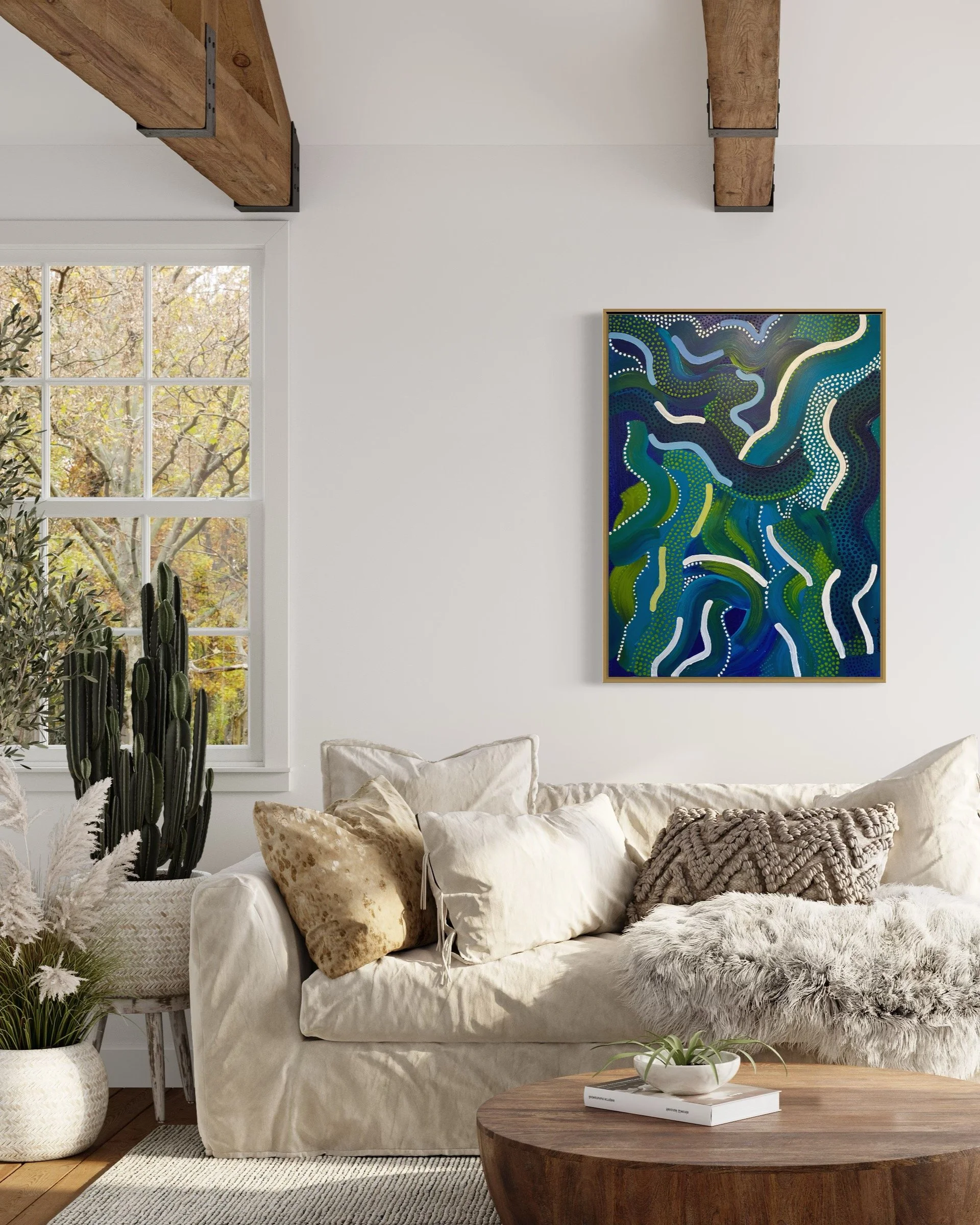 Living room with beige couch, decorative pillows, abstract painting, wooden coffee table, plants by the window, and exposed wooden beams.