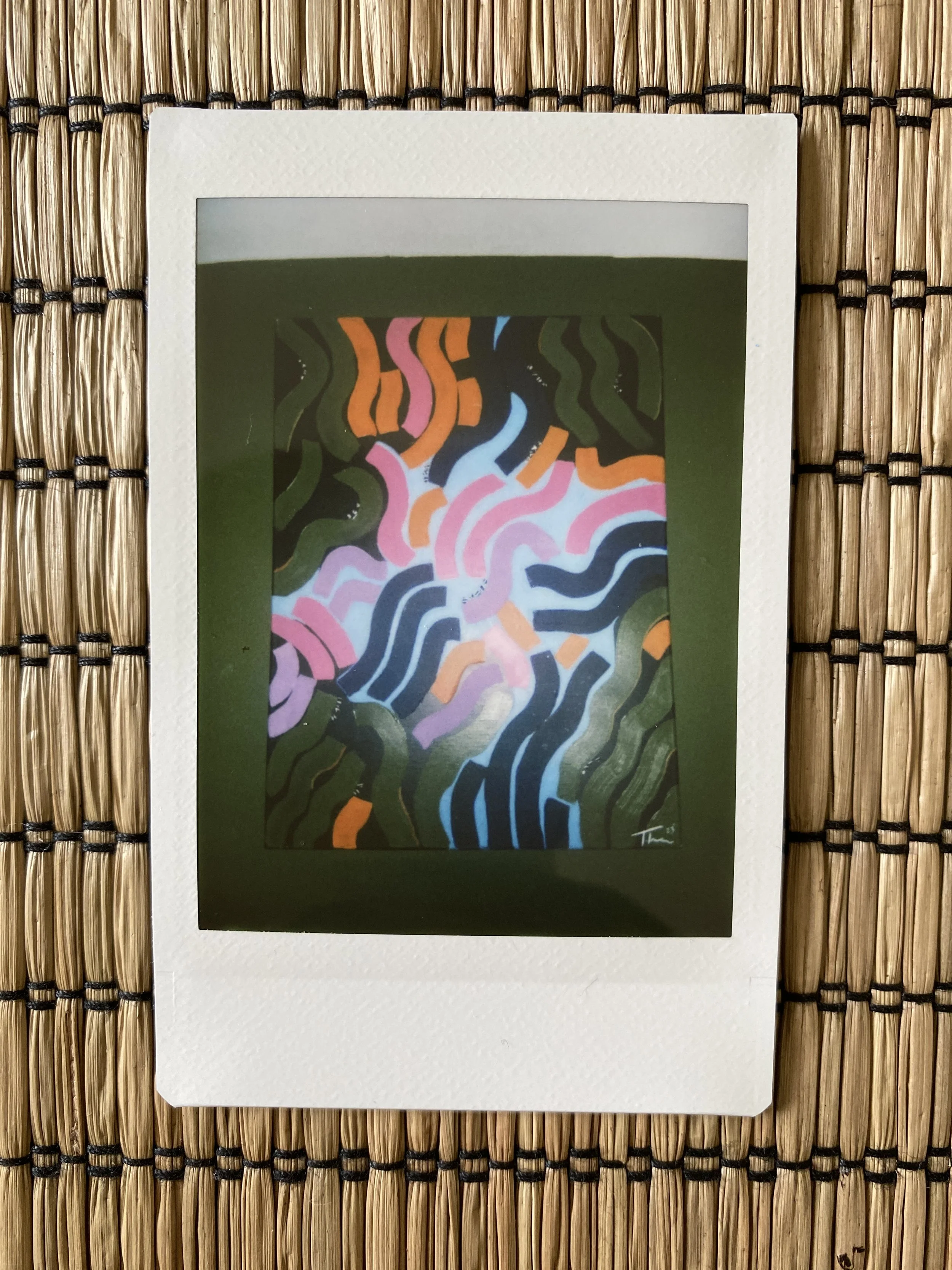 Polaroid photo of abstract colorful wavy lines on wicker mat