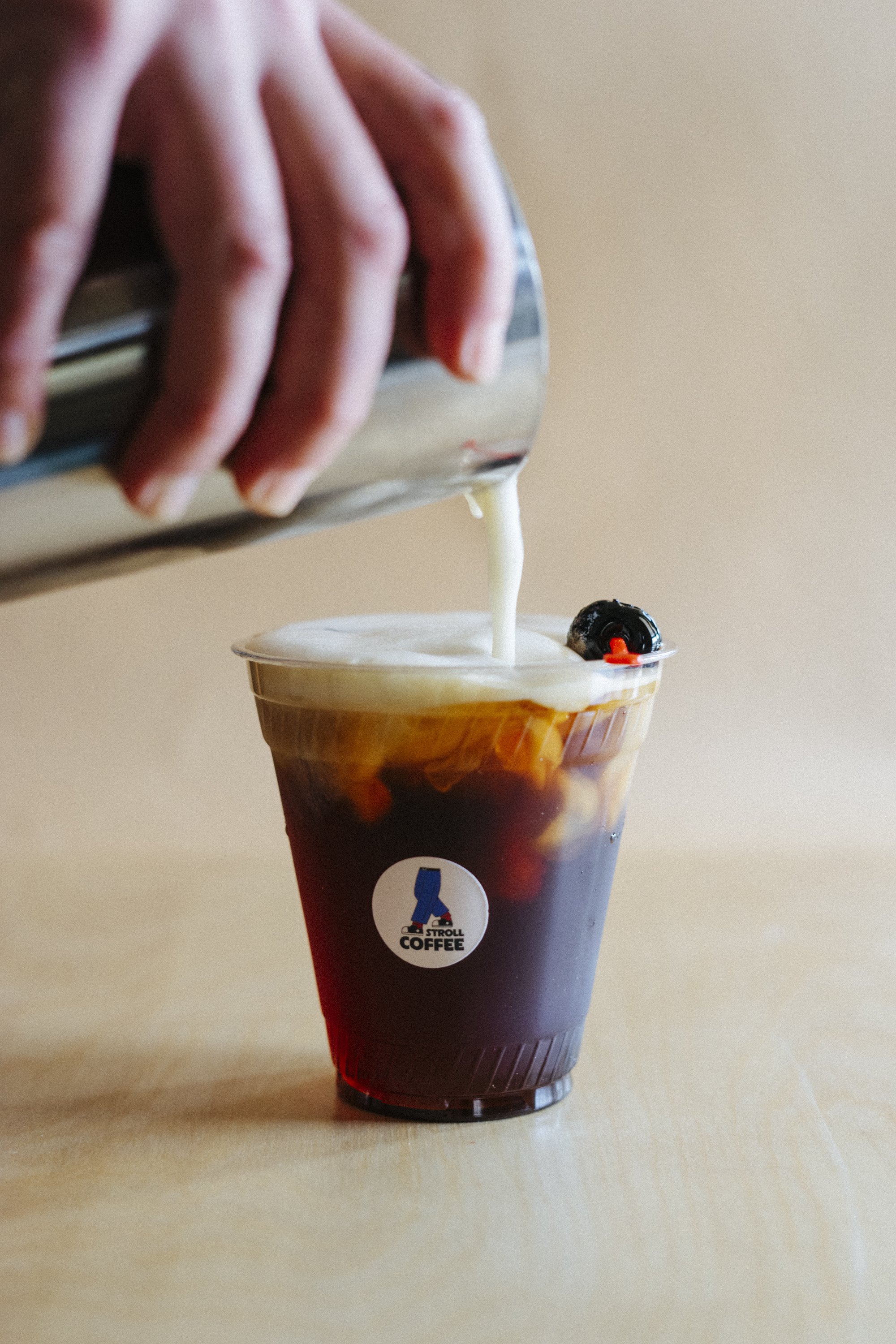 A cold brew coffee in a plastic cup with cream being poured from a metal pitcher.