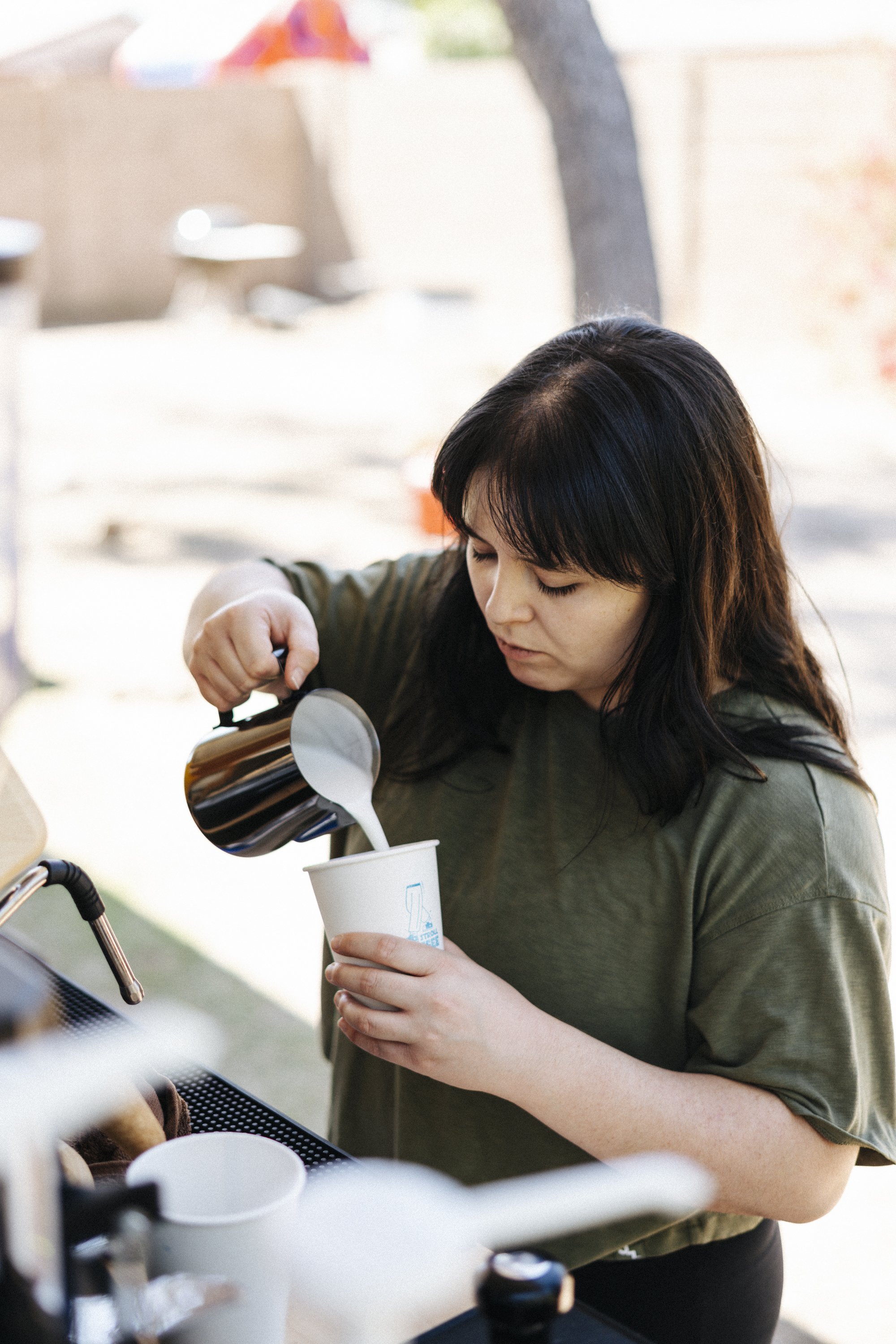 Barista pouring milk into a cup outdoors