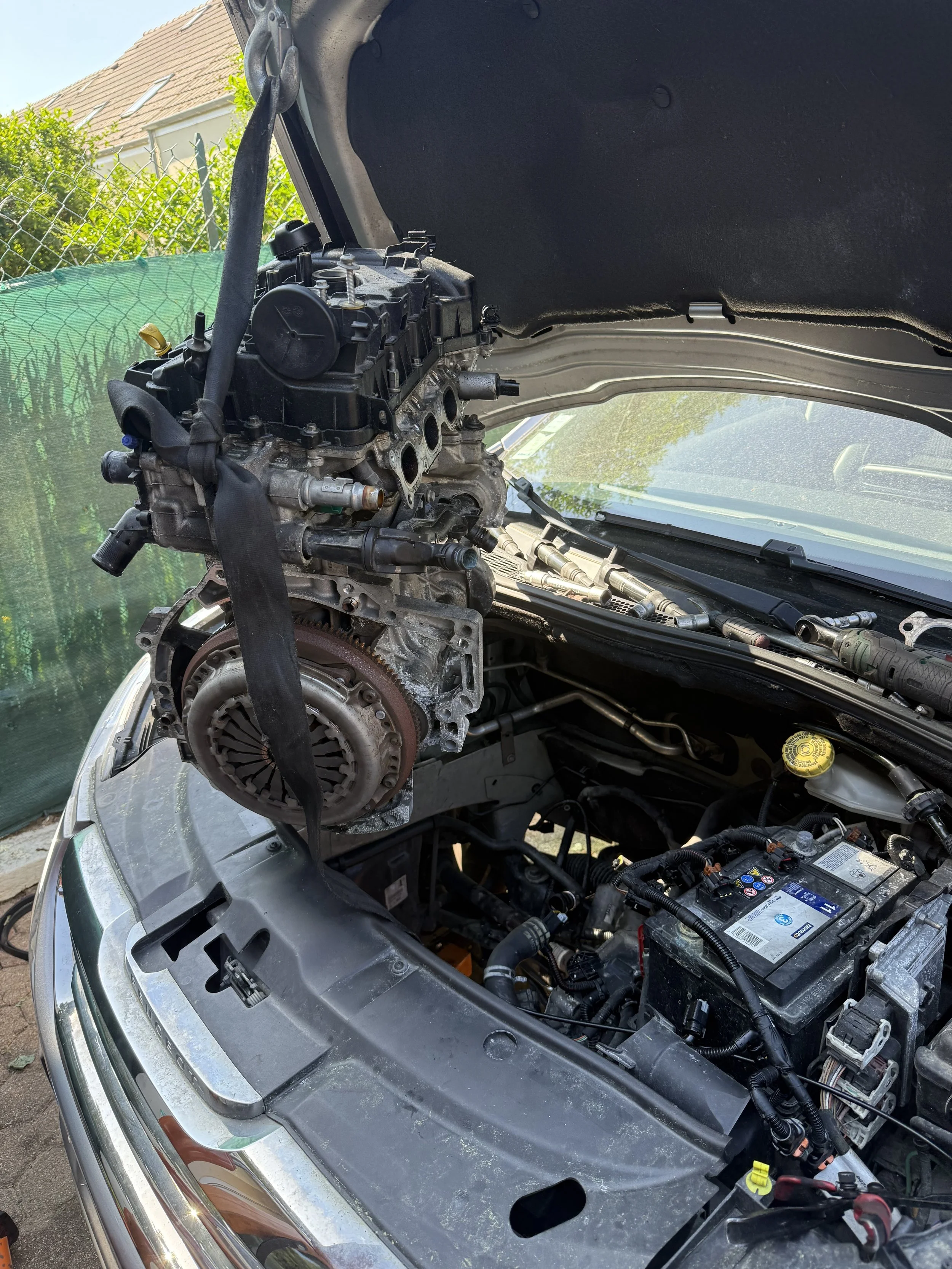 Le capot d'une voiture est ouvert, révélant le moteur puretech en cours de réparation ou de maintenance, avec divers composants mécaniques et électriques visibles.