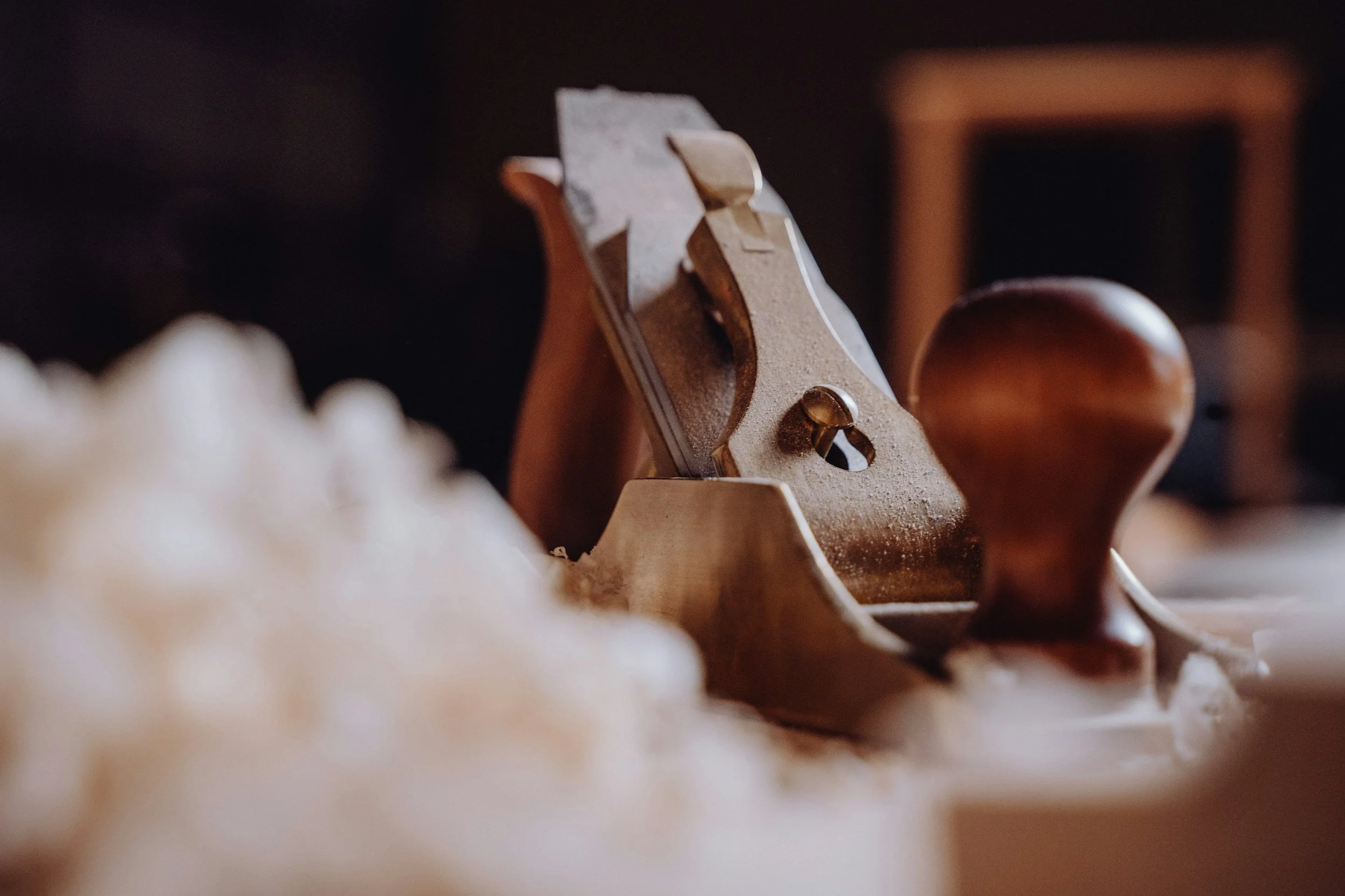 A vintage wooden hand plane tool on a workbench, with wood shavings in the foreground.