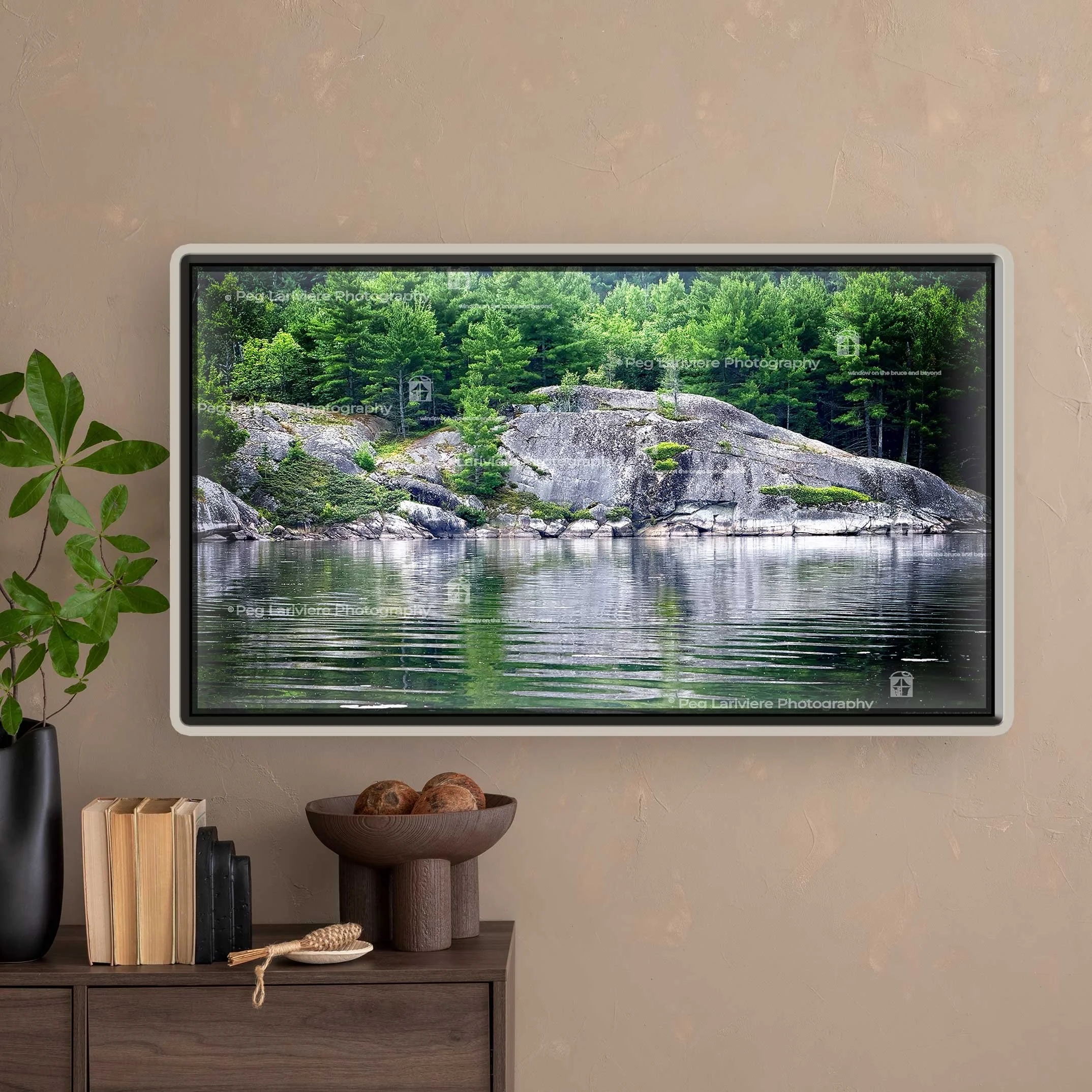 A wooden console sits beneath the picture of Serpent Harbour. It has books, a black vase, a sculptural bowl of natural objects, and a wooden scoop. Next to it sits a potted plant.