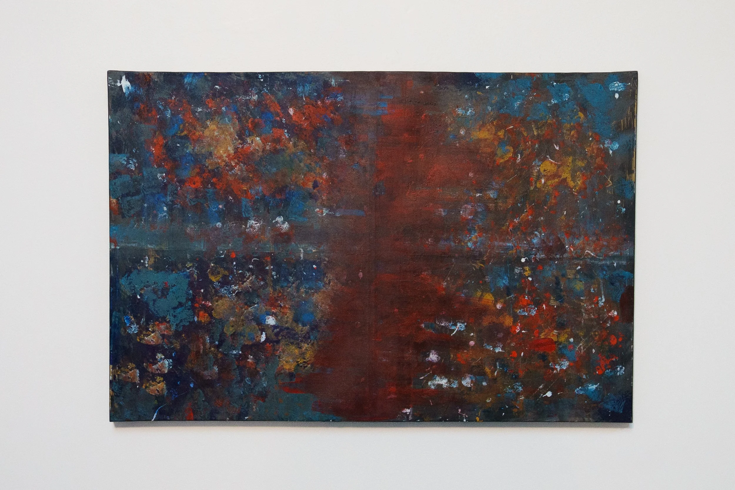 Abstract painting with dark red, blue, orange, and yellow splashes on canvas, hung on a white wall.