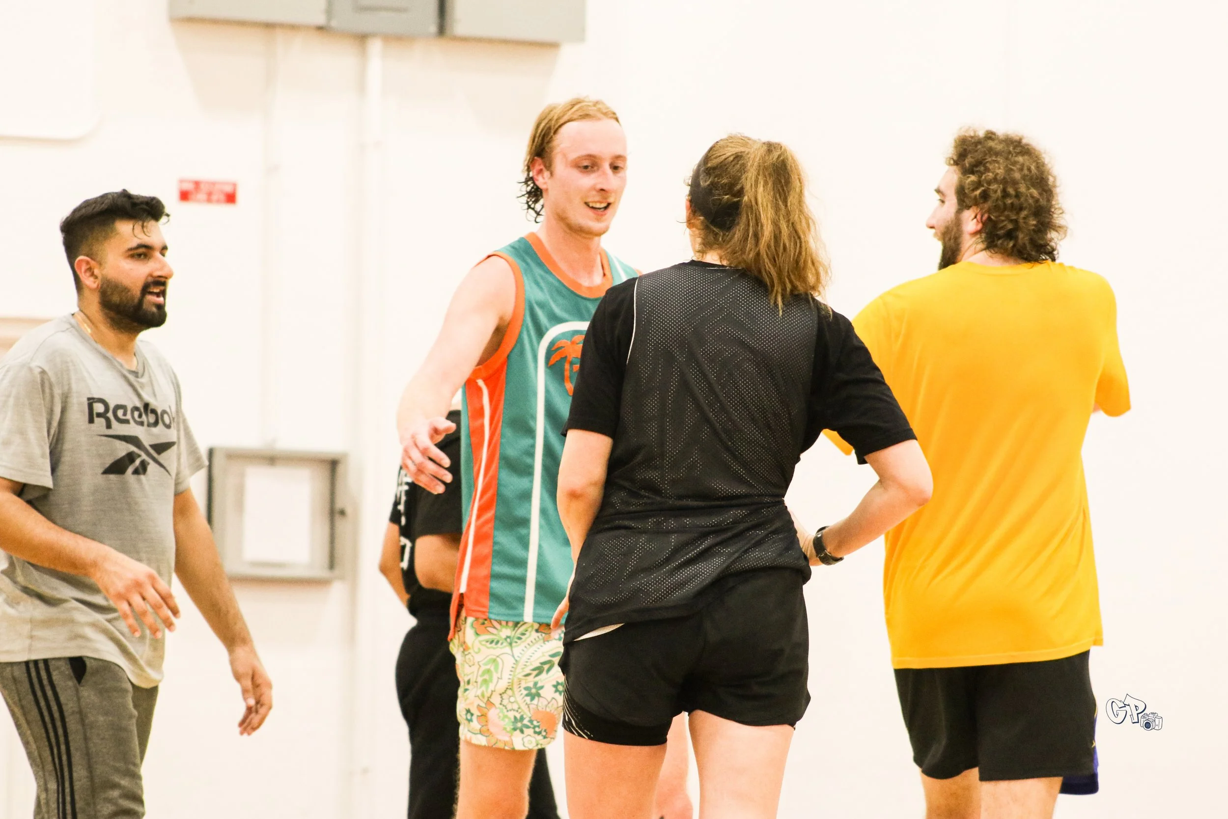 Group of four young adults talking and smiling indoors, two men and two women, casual athletic clothing, engaging in friendly conversation.