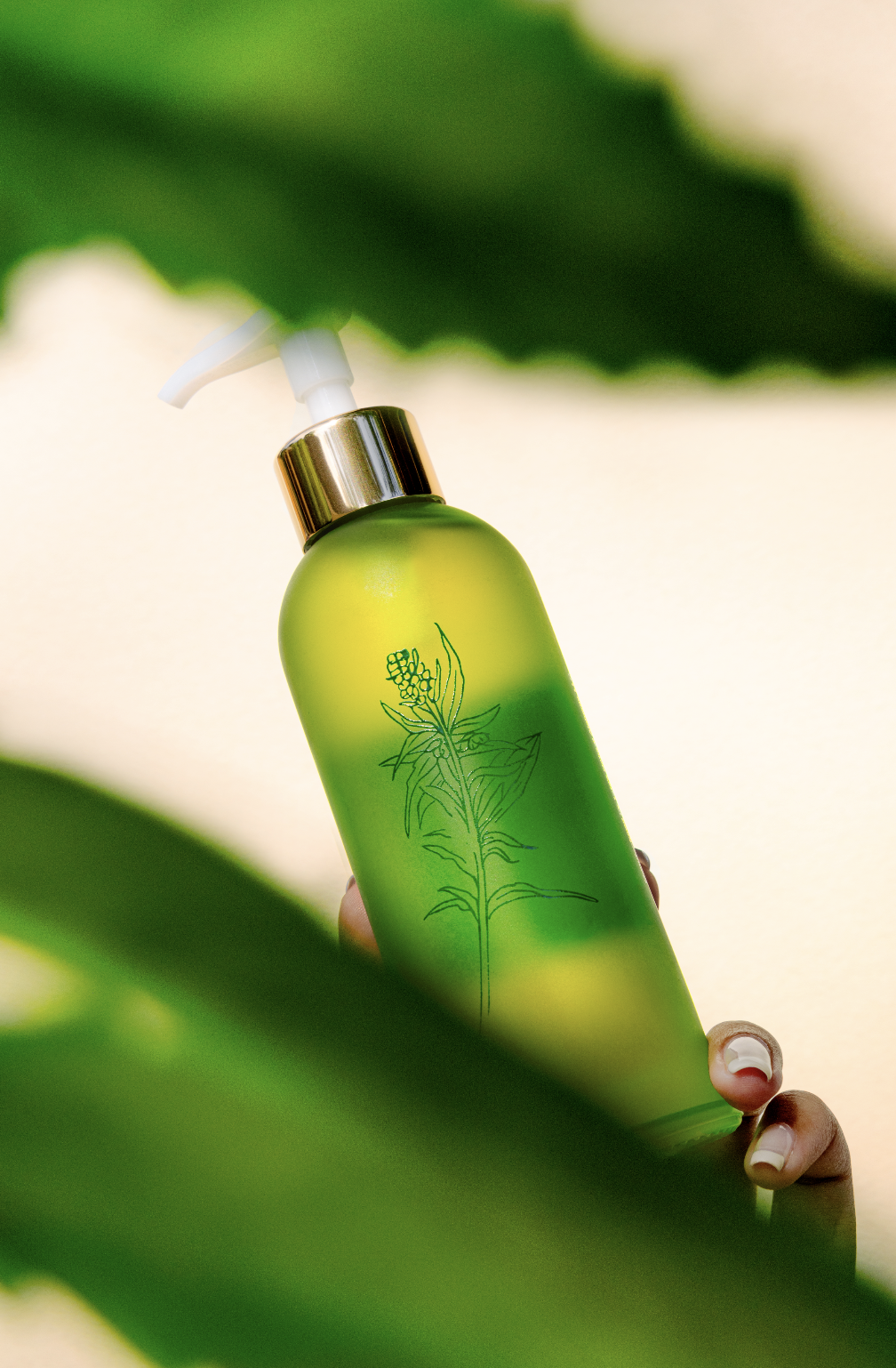 A green pump bottle with a botanical illustration on it, held partially behind green leaves.