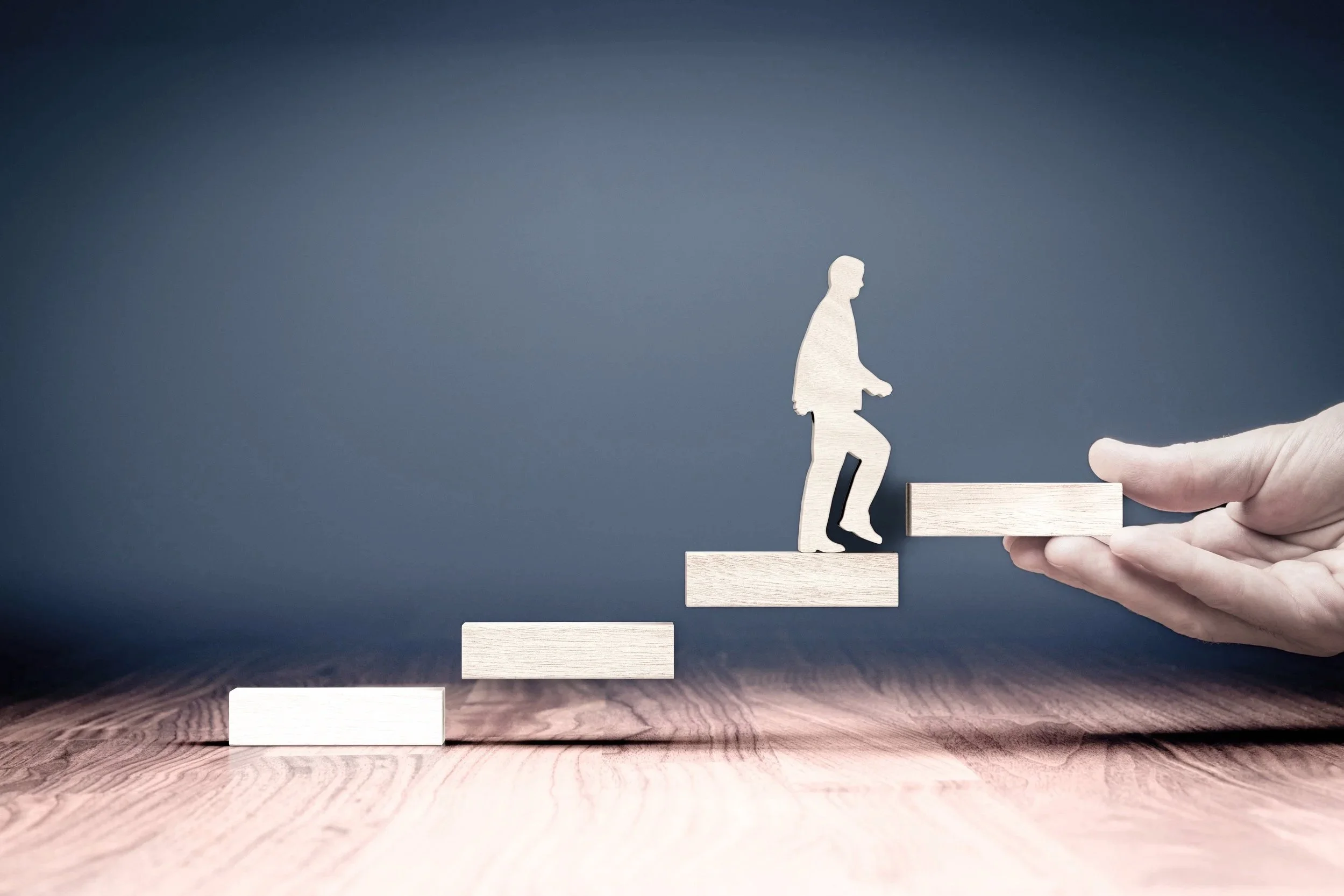 A hand holding a wooden ramp supporting a silhouette of a person stepping up, symbolizing progress or personal growth.