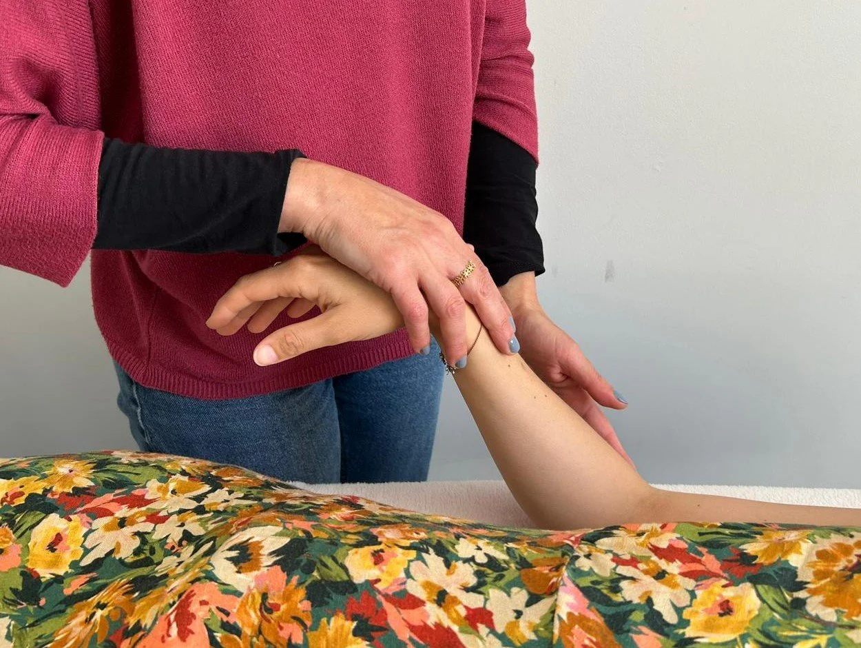 Une personne effectue un massage de l'avant-bras d'une autre personne sur une table avec un drap à motif floral.