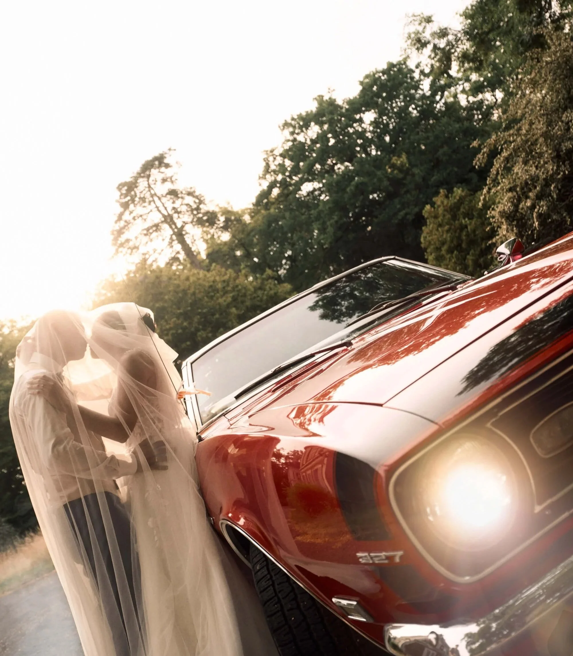 un couple qui s'embrasse sur une voiture de sport vintage lors de leur mariage