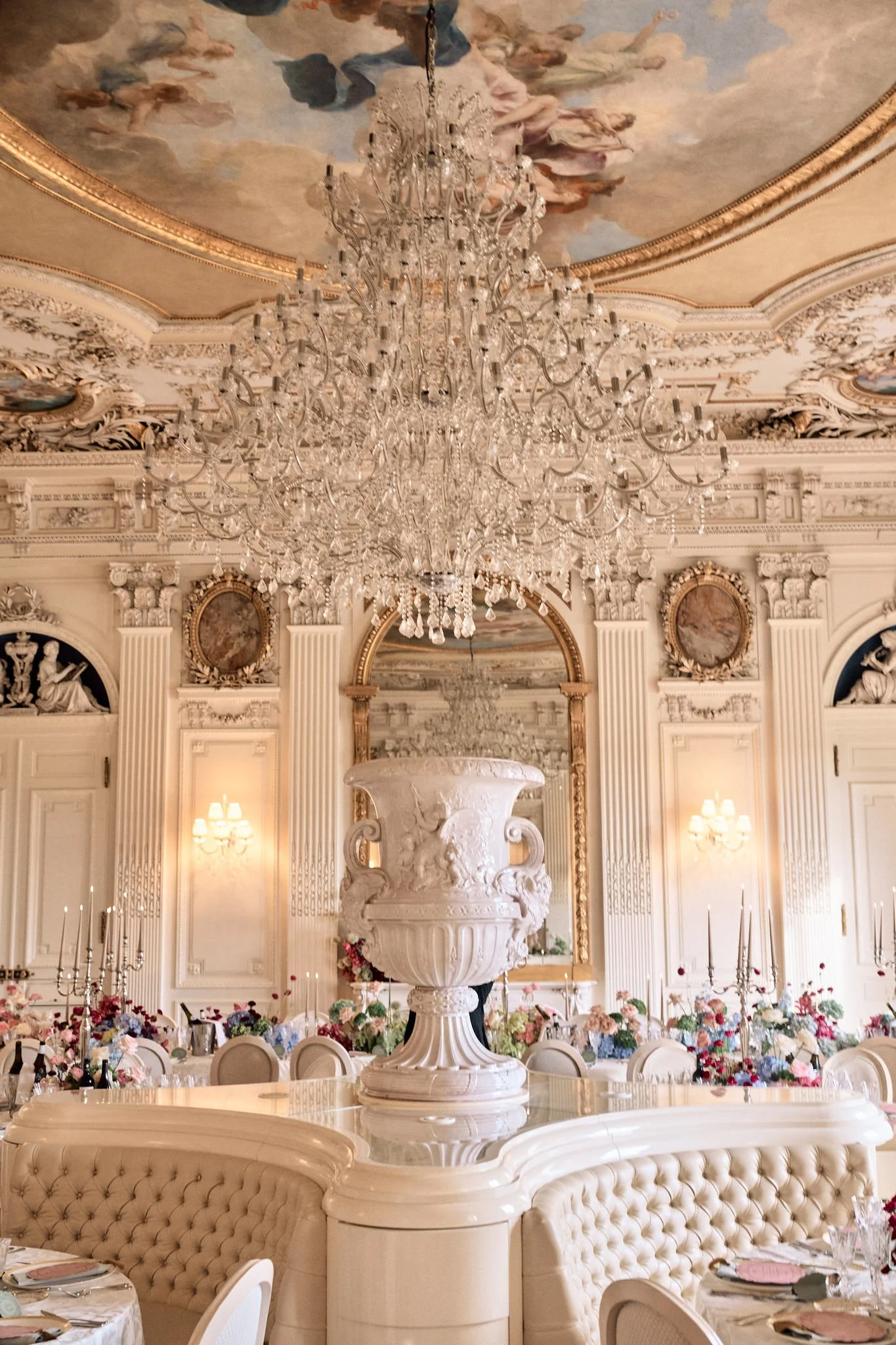 Une salle de réception élégante avec un plafond peint, un lustre en cristal et une décoration baroque, prête pour un événement ou un dîner formel.