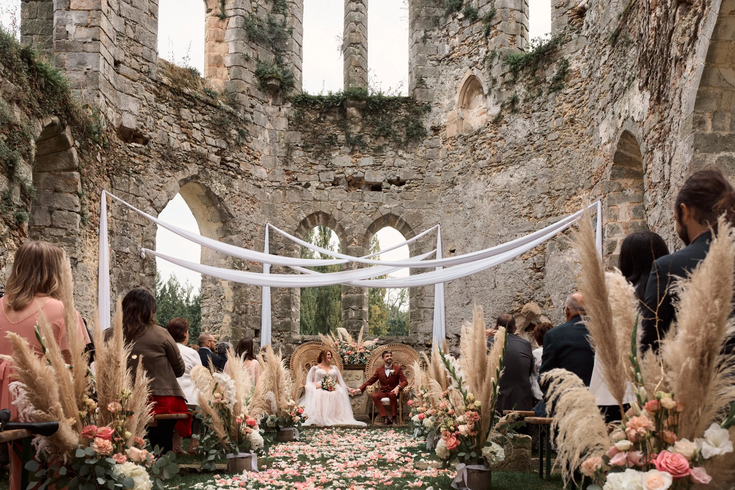 Cérémonie de mariage dans un vieux bâtiment en ruines avec des caissons blancs, des fleurs et des invités assis.