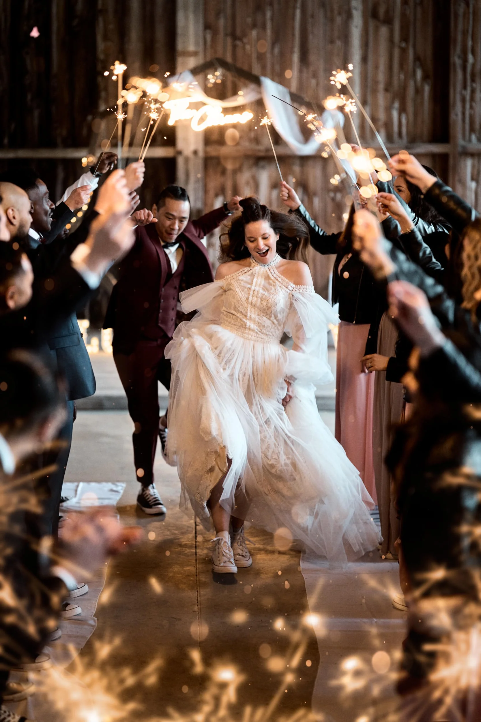 Un groupe de personnes fête un mariage avec des feux d'artifice et des sparklers, la mariée en robe blanche danse au centre.