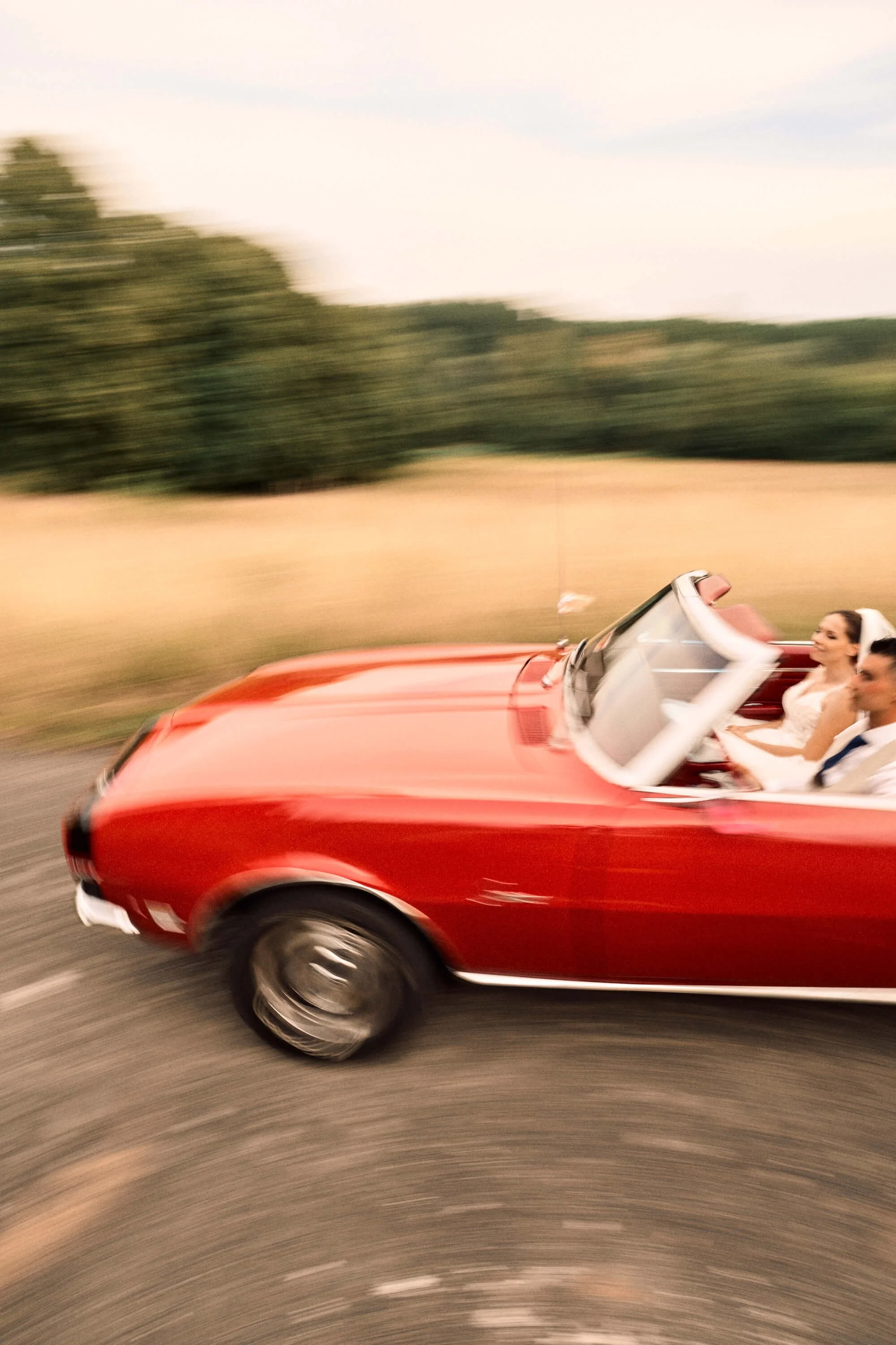 un couple en tenue de mariage dans une mustang rouge