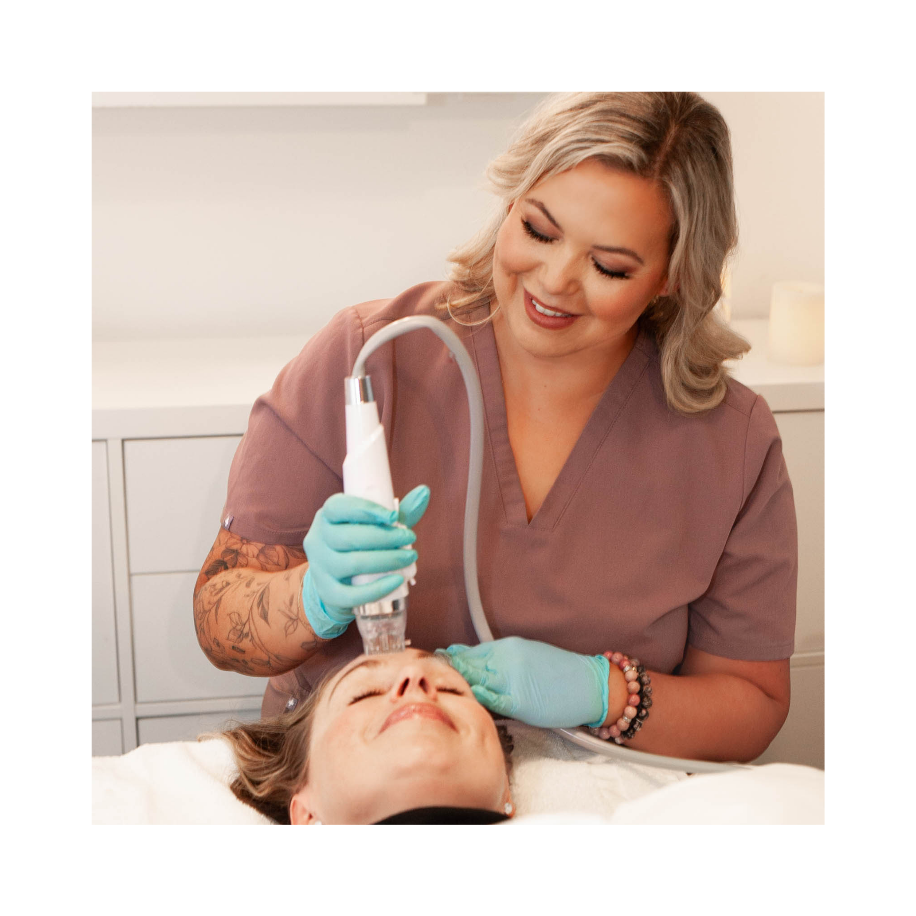 A woman in medical scrubs using a laser treatment device on a woman's forehead in a clinical setting.