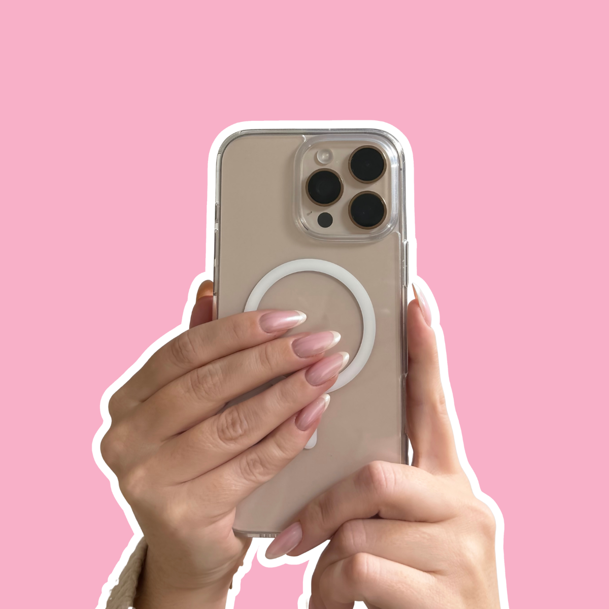 Person holding a smartphone with a clear case and a white ring grip, against a pink background.