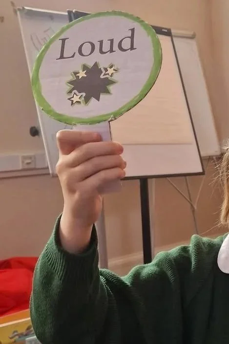 Pupil at after school club music class holding up a sign that reads 'loud'