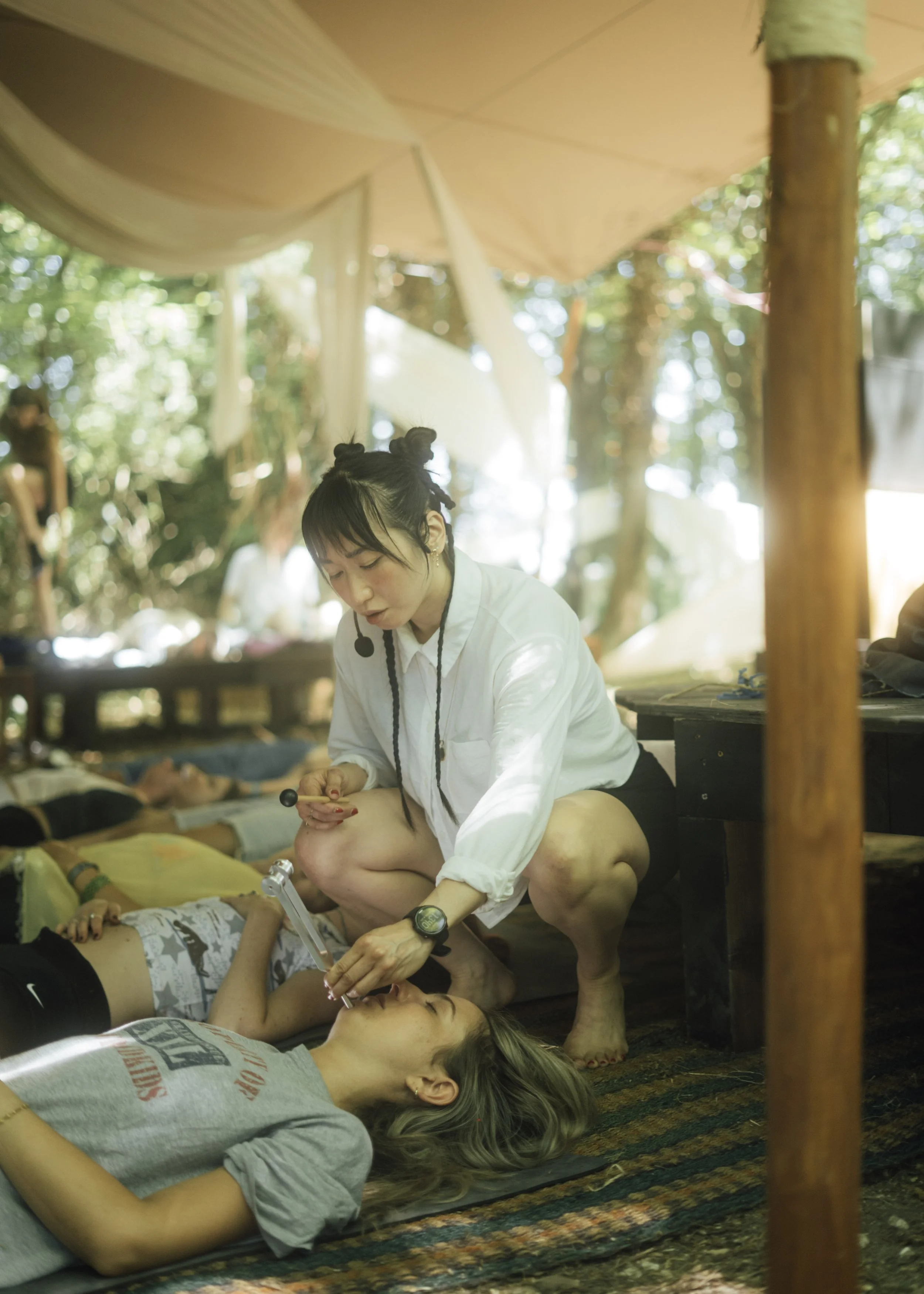 Sound Mirror is playing a tuning fork on a young woman who is lying down on a yoga mat next to others at a gong bath.