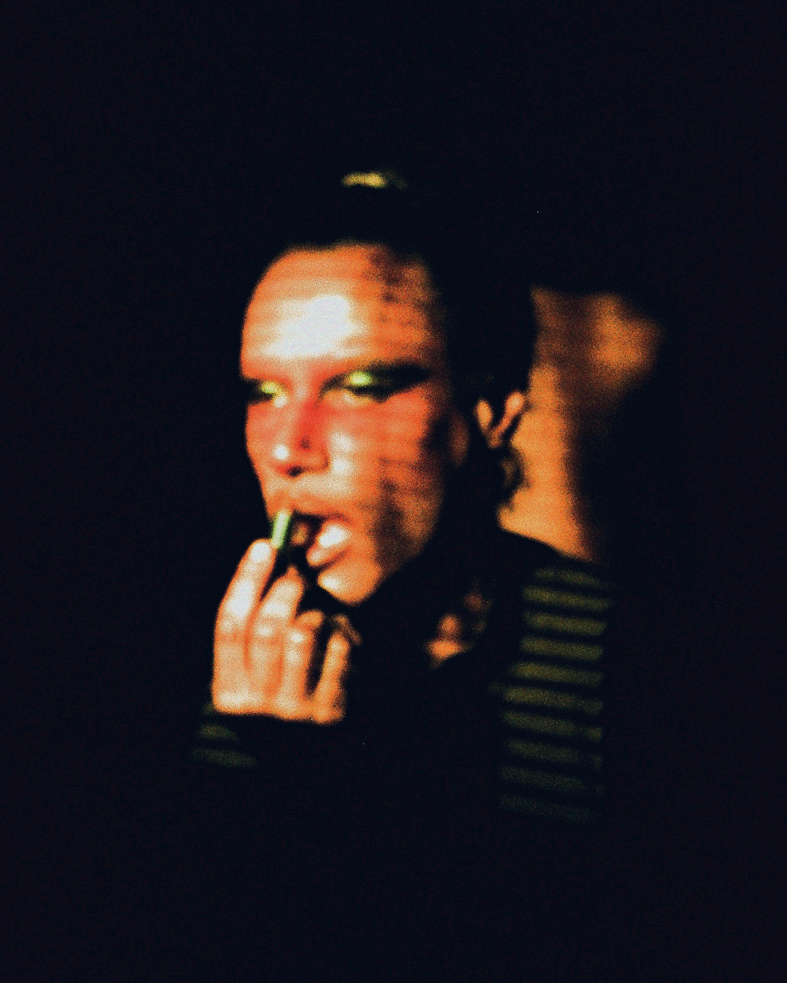 Image of Voxgima Lo applying lipstick with blurry orange lighting on film
