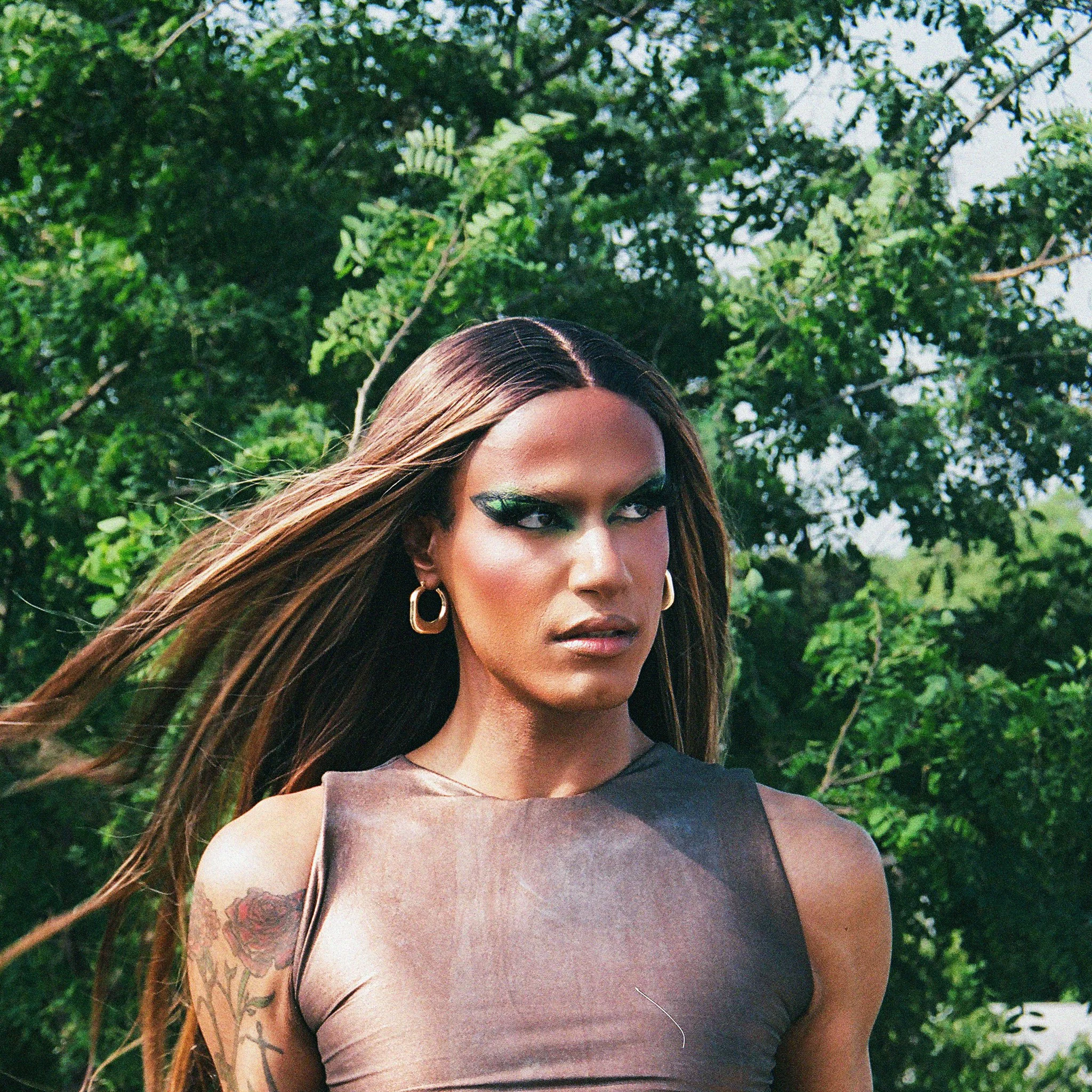 Image of a drag artist wearing a brown top with a green tree on film