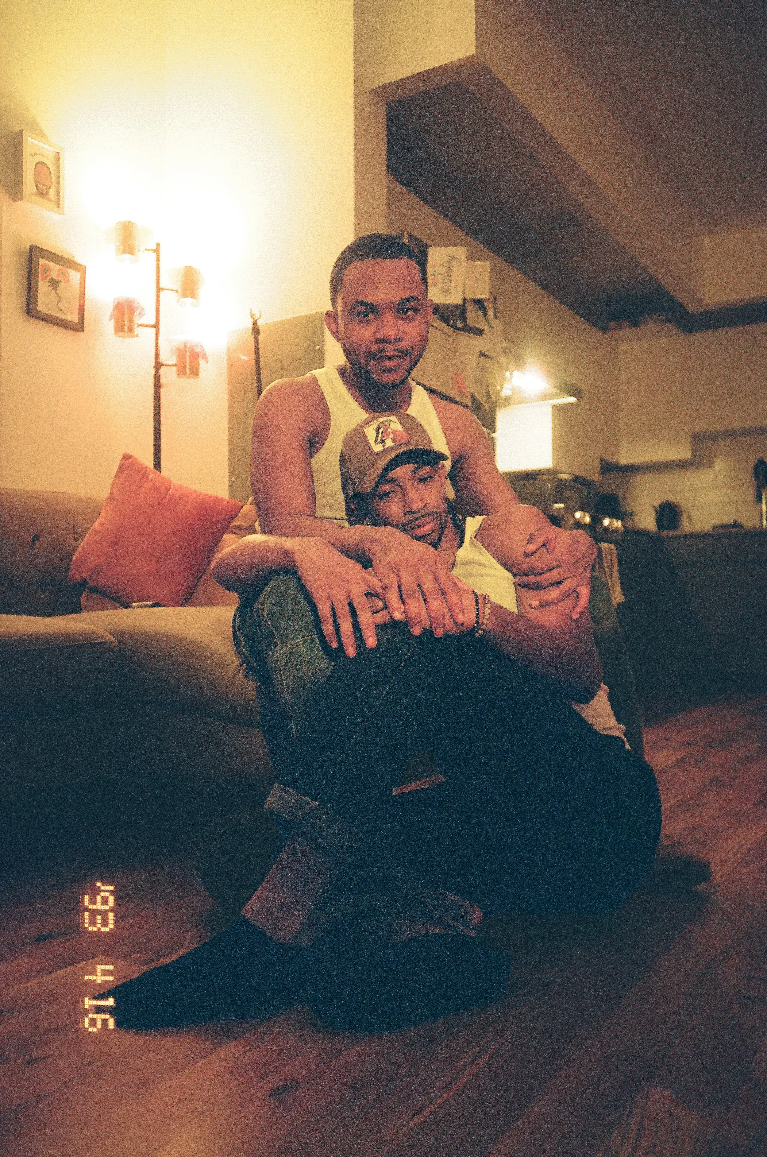 Image of a black gay couple cuddling on a couch shot on film