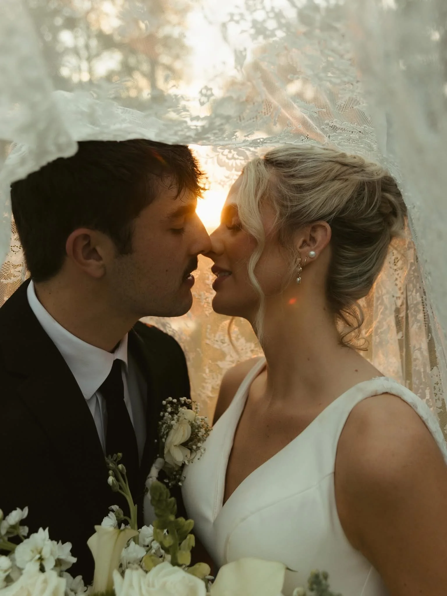 Close-up of a bride and groom holding hands while dancing at their wedding. The bride is wearing a lace wedding dress, and the groom is in a dark tuxedo.
