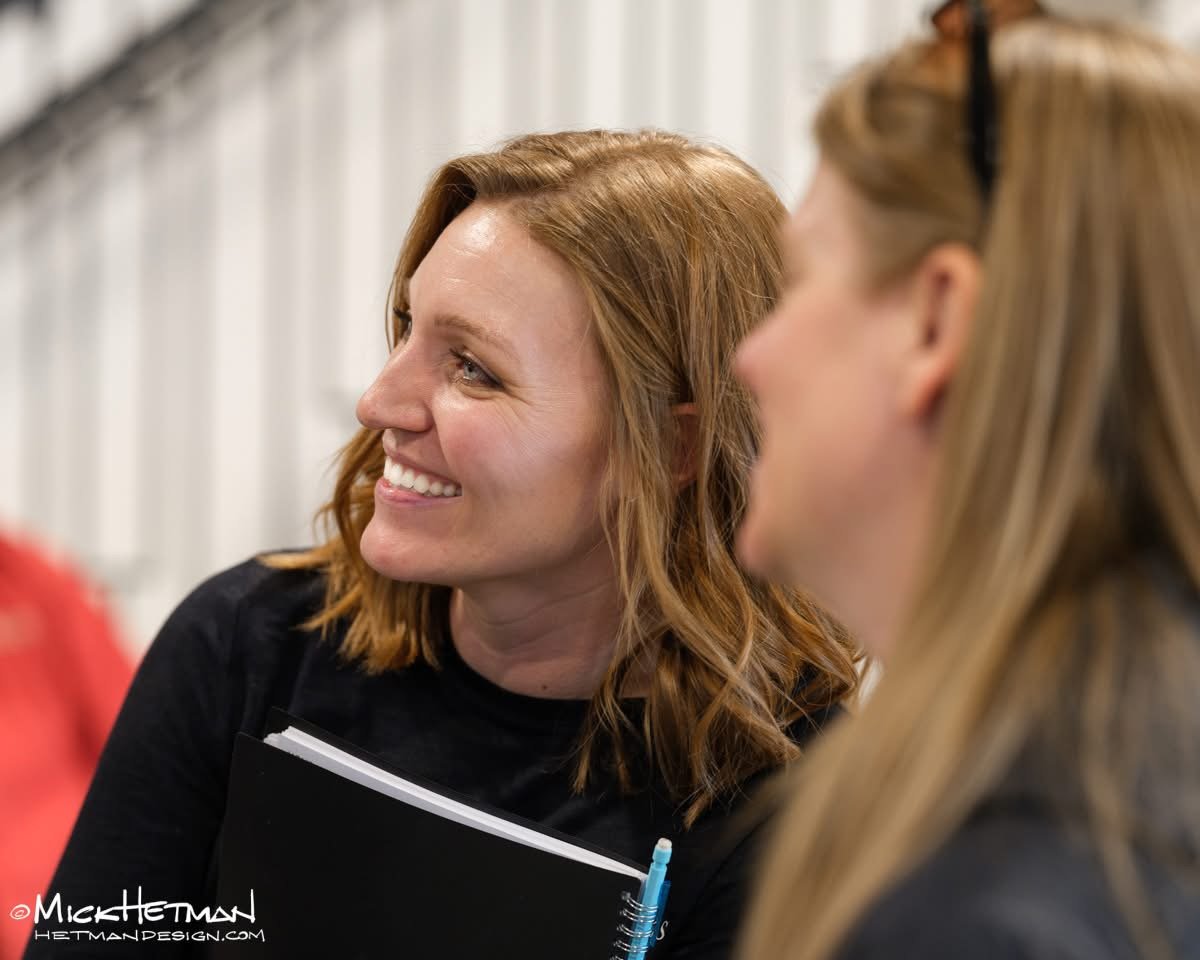 Two women having a conversation, one with red hair smiling, the other with blonde hair, in a casual setting.