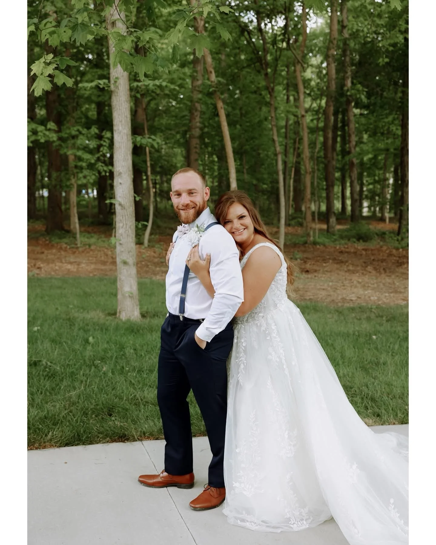 Close-up of a bride and groom holding hands outdoors, with the bride wearing a lace gown and the groom in a black suit.