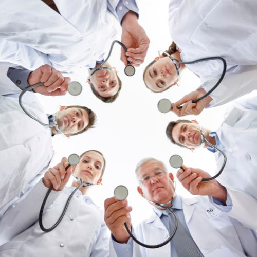 Group of doctors and medical professionals standing in a circle, holding stethoscopes and looking down towards the camera.
