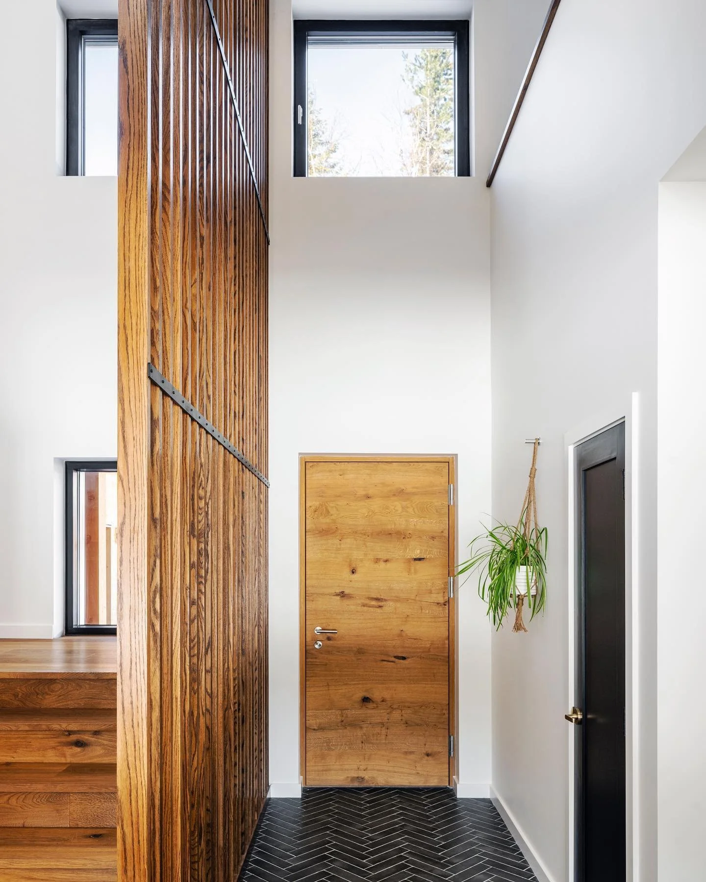 Modern interior with a custom wood door, vertical wooden slat partition, high ceilings, and minimalist design in a bright entryway.