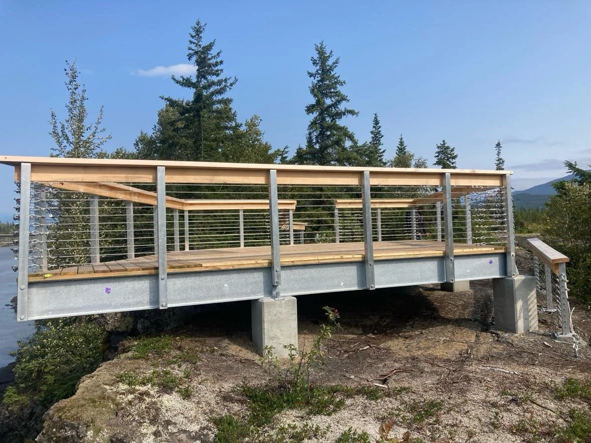side view of a outdoor wood deck with a custom handrail built on a granite slab in Squamish with old pine behind