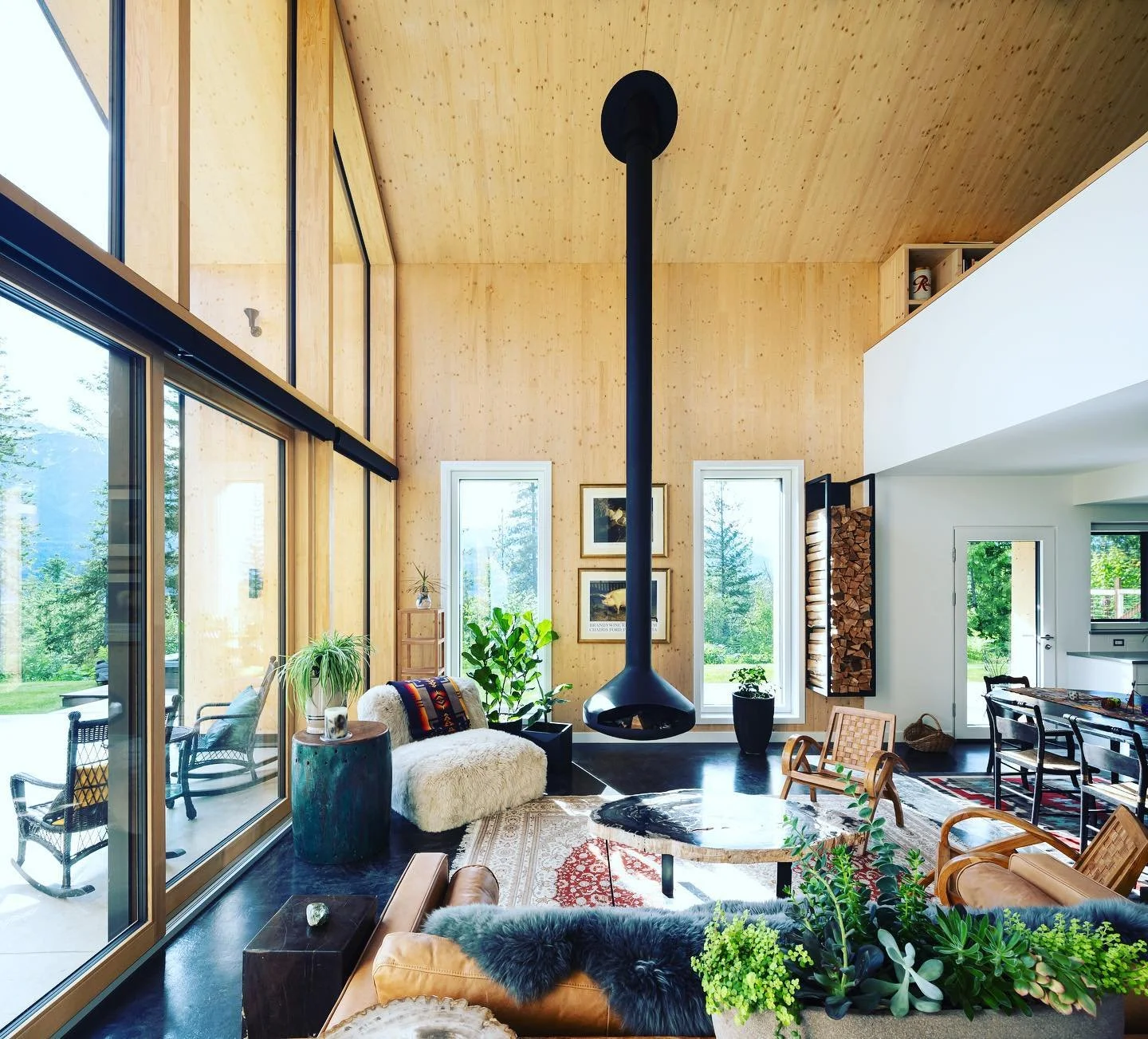 modern living room with a black proeminent chimney in the middle with cosy furniture and all wooden wall and ceiling