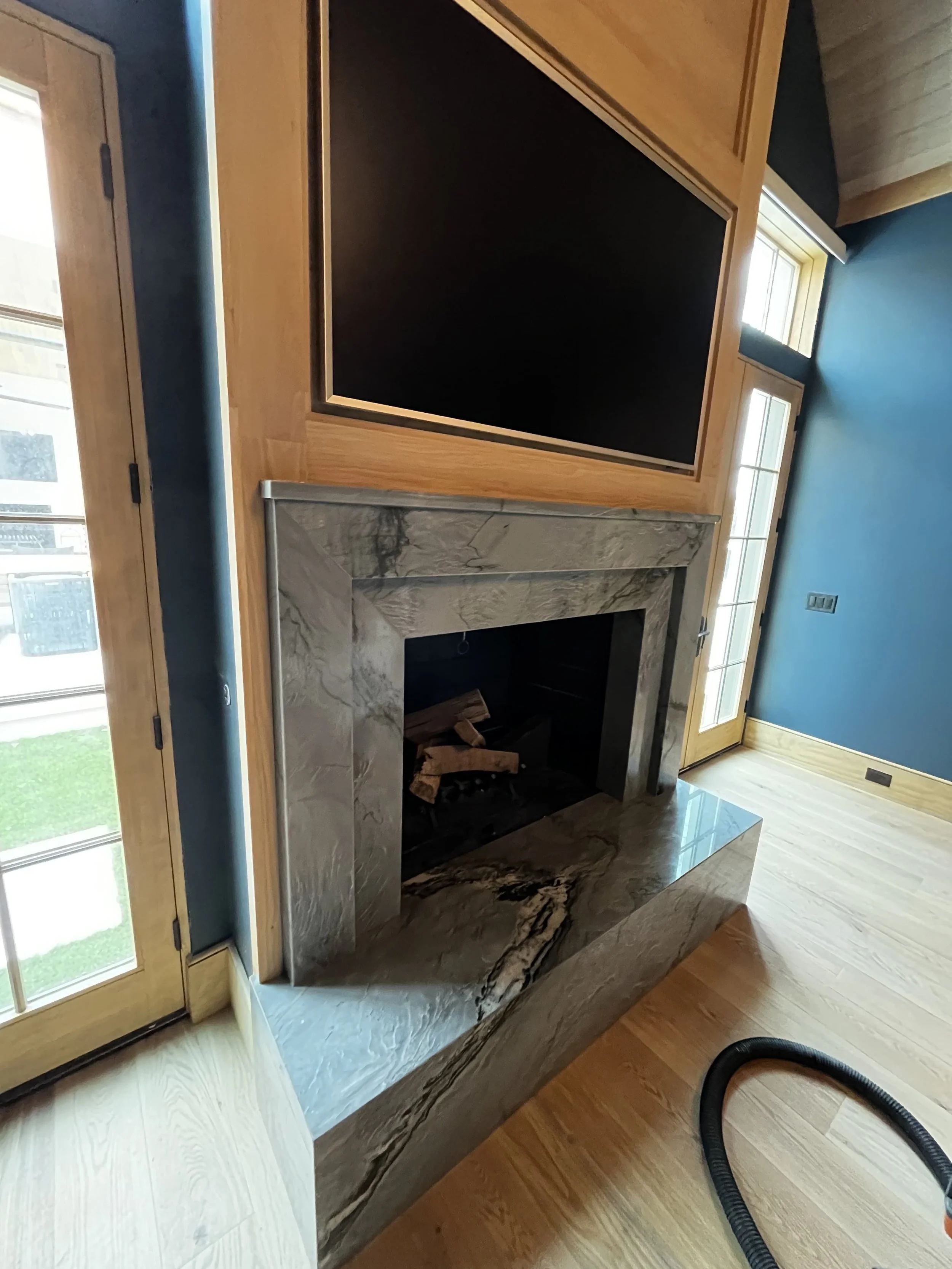 Living room with a TV mounted above a fireplace with marble surround, wooden side doors, a blue wall, and hardwood flooring.