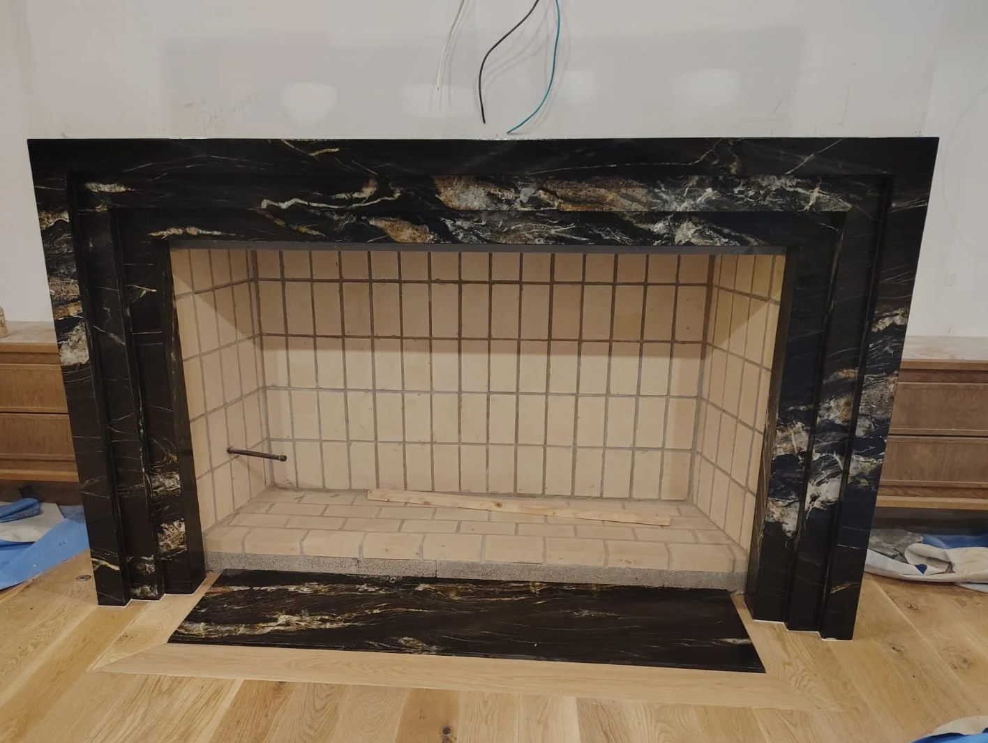 Empty fireplace with black marble surround and beige tiled interior, installed in a room with a wood floor.
