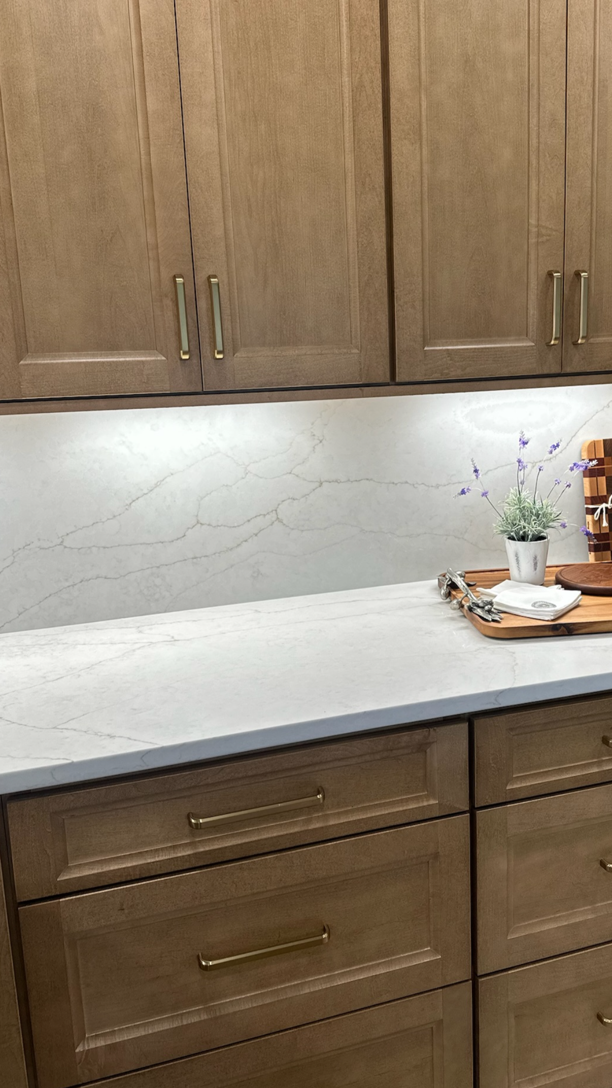 Kitchen with wooden cabinets, white marble countertop and backsplash, small potted plant with purple flowers on a wooden tray
