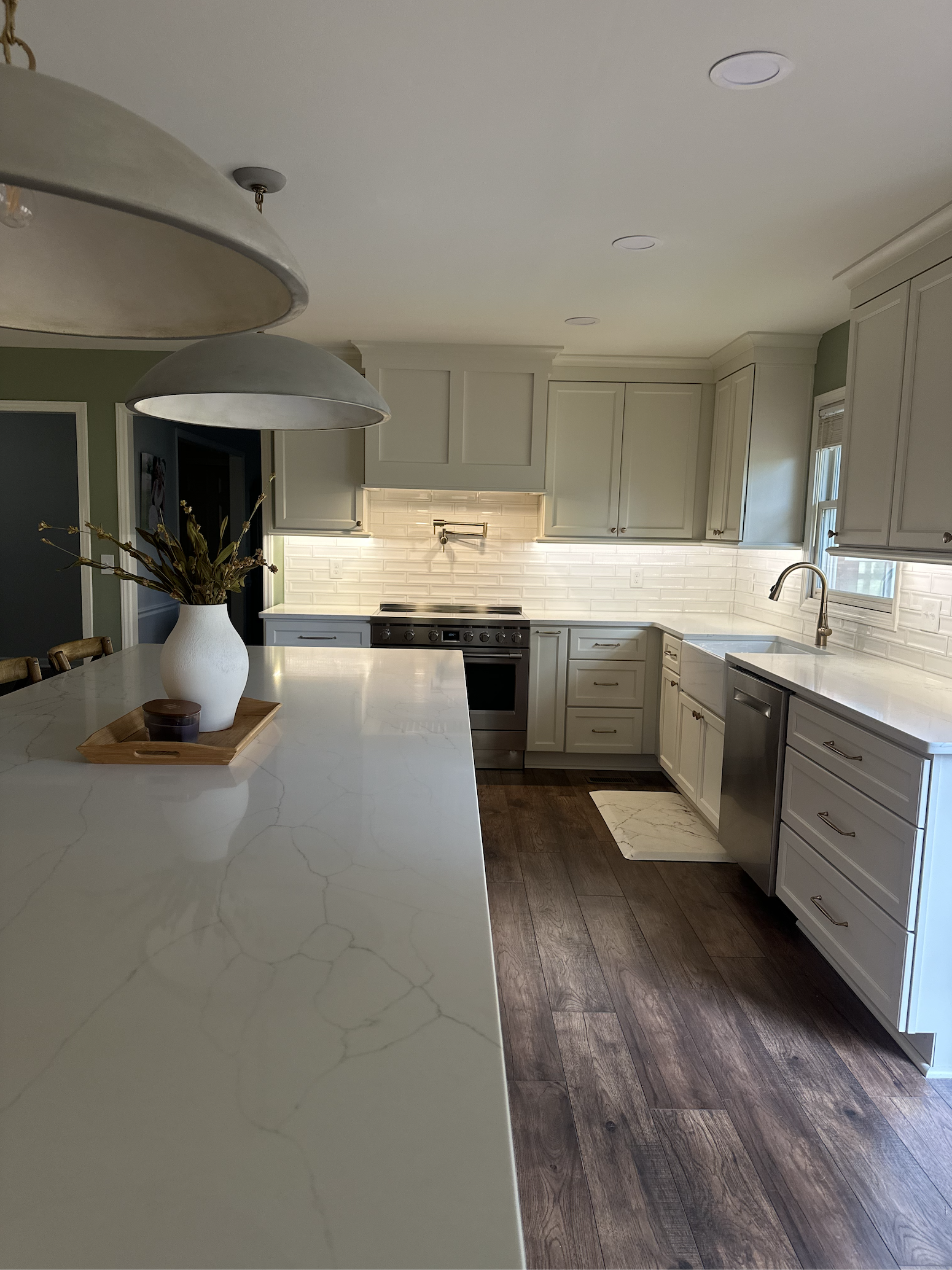 Modern white kitchen with marble countertops, wooden cabinets, stainless steel appliances, a vase with flowers on the island, and dark wooden flooring.