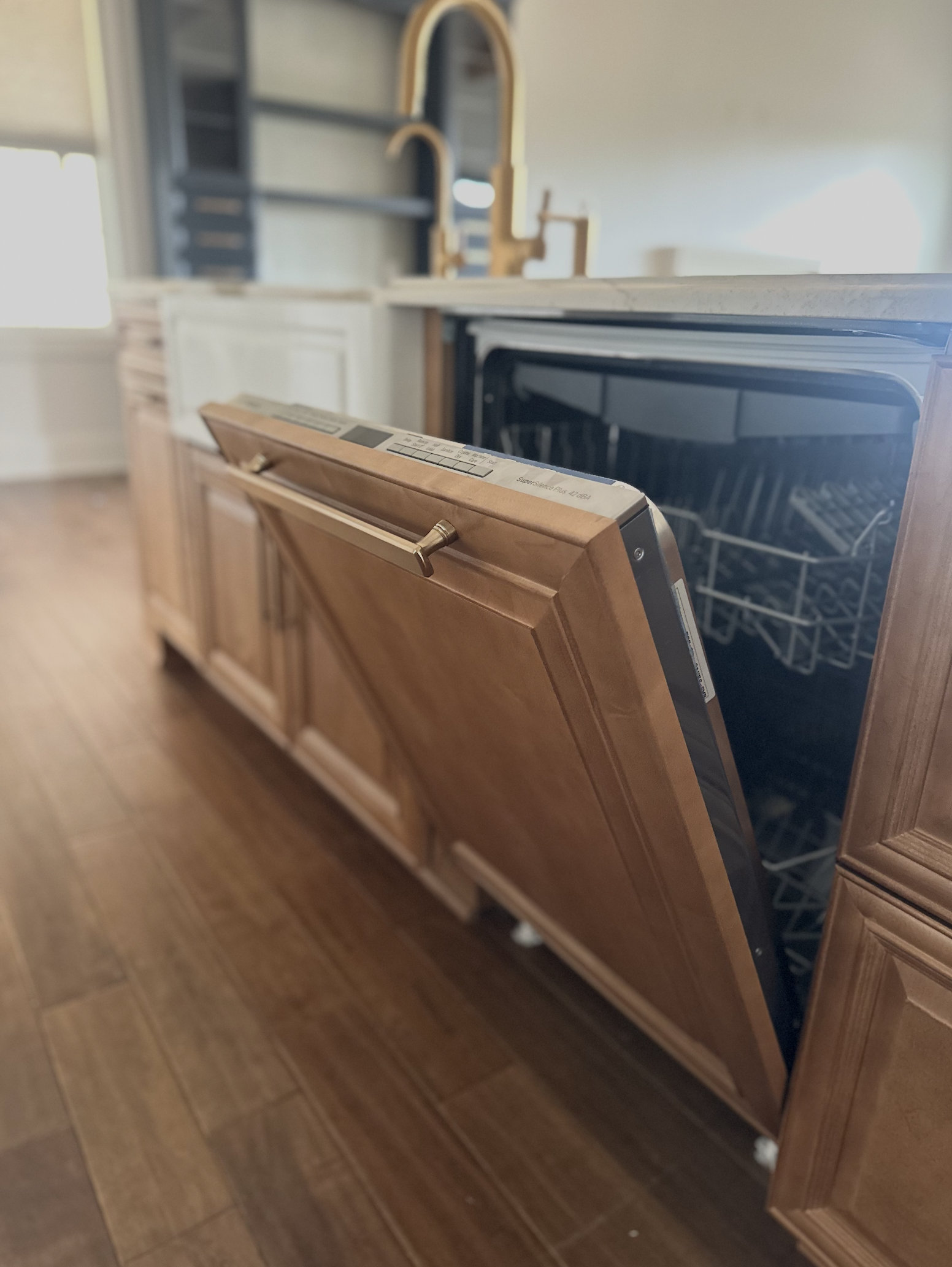 A dishwasher with a wooden front panel in a kitchen with wooden cabinets and flooring.