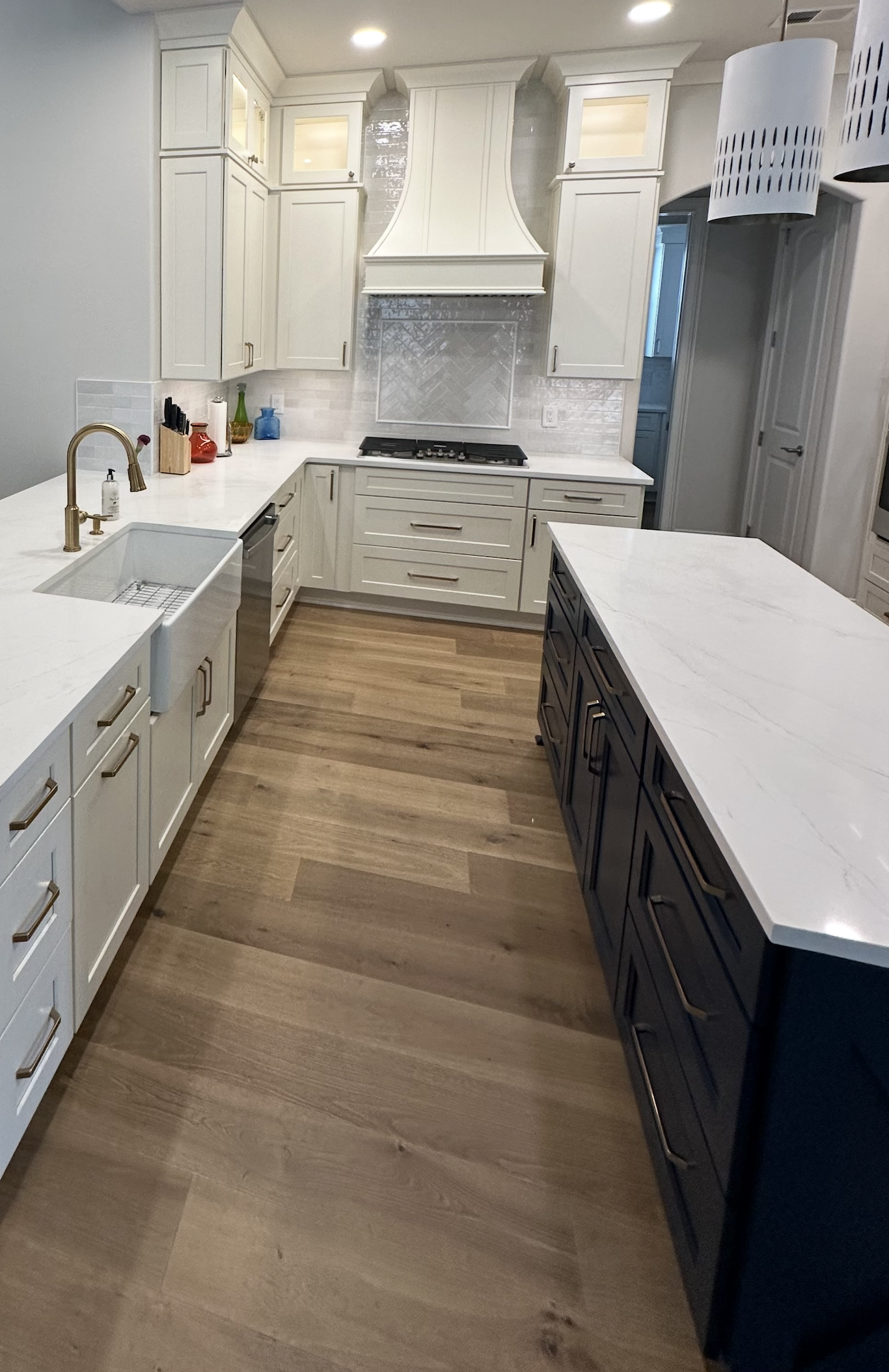 Modern kitchen with white cabinets, a kitchen island with dark blue drawers, wood flooring, and stainless steel appliances, including a built-in oven and gas stove.