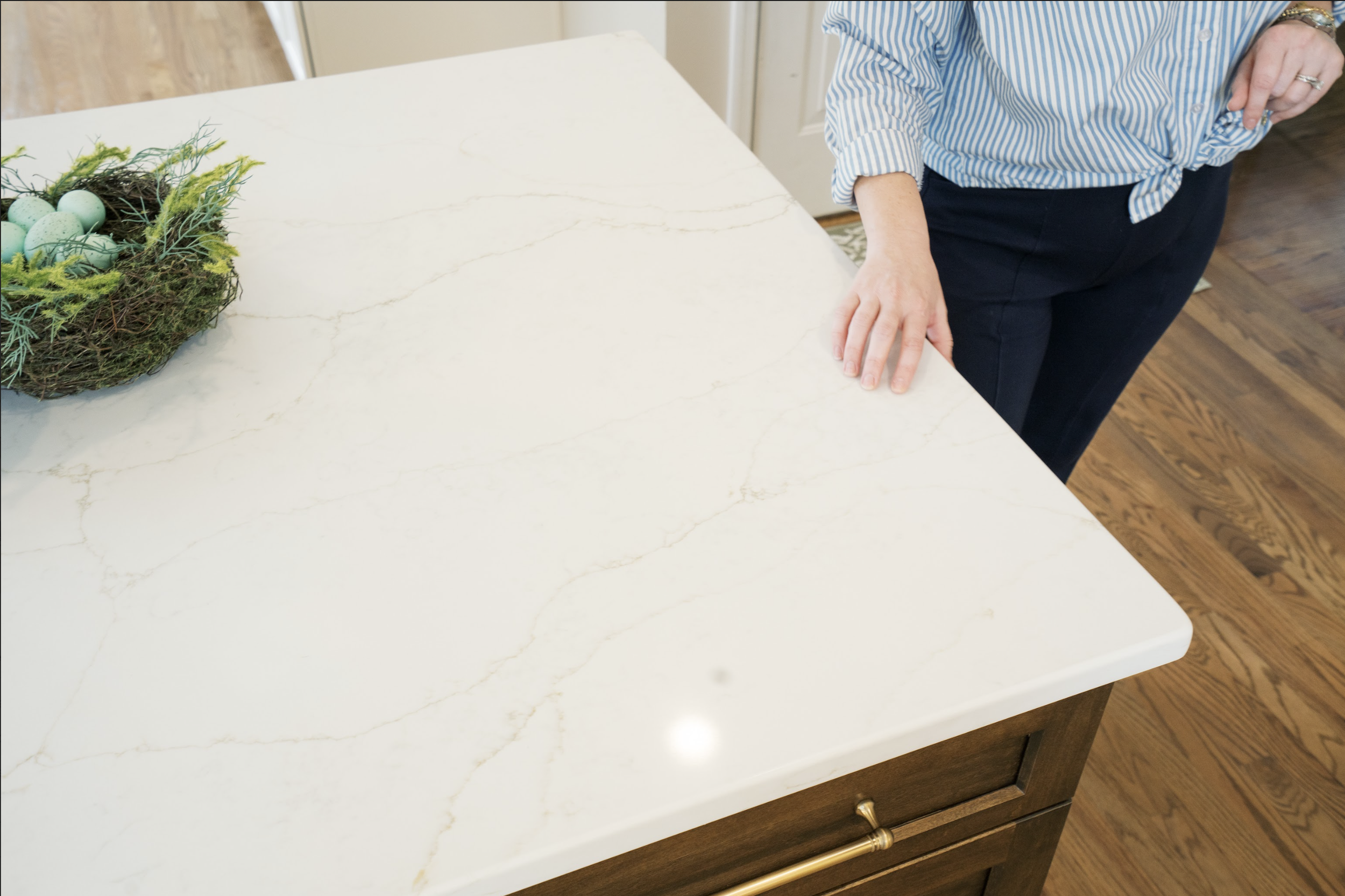 Person standing near a kitchen island with a white marble countertop and a decorative nest with blue eggs