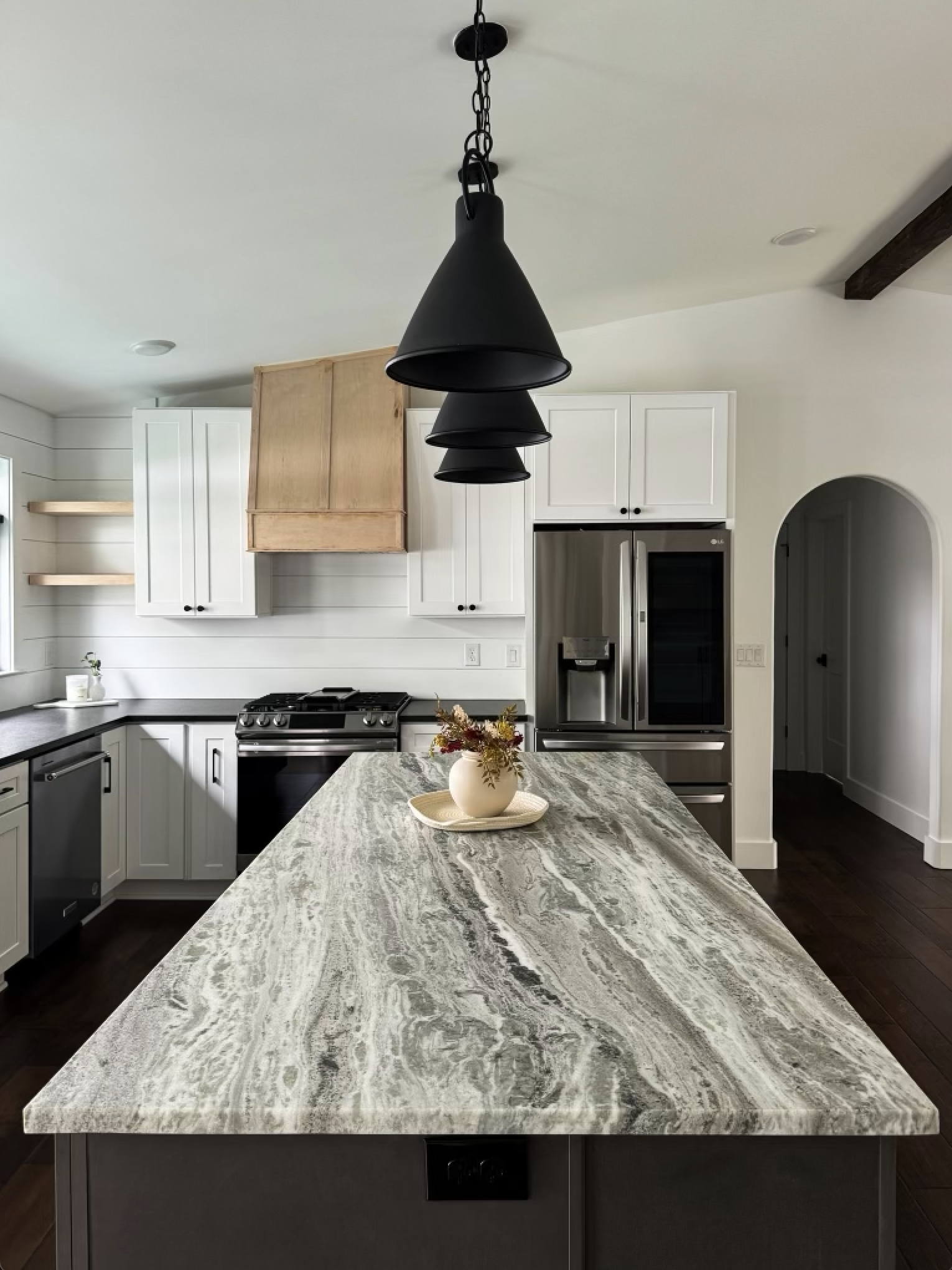 Modern kitchen with a large marble island, white cabinets, stainless steel refrigerator, black stove, and black pendant lights hanging above the island, with a small flower arrangement on top.