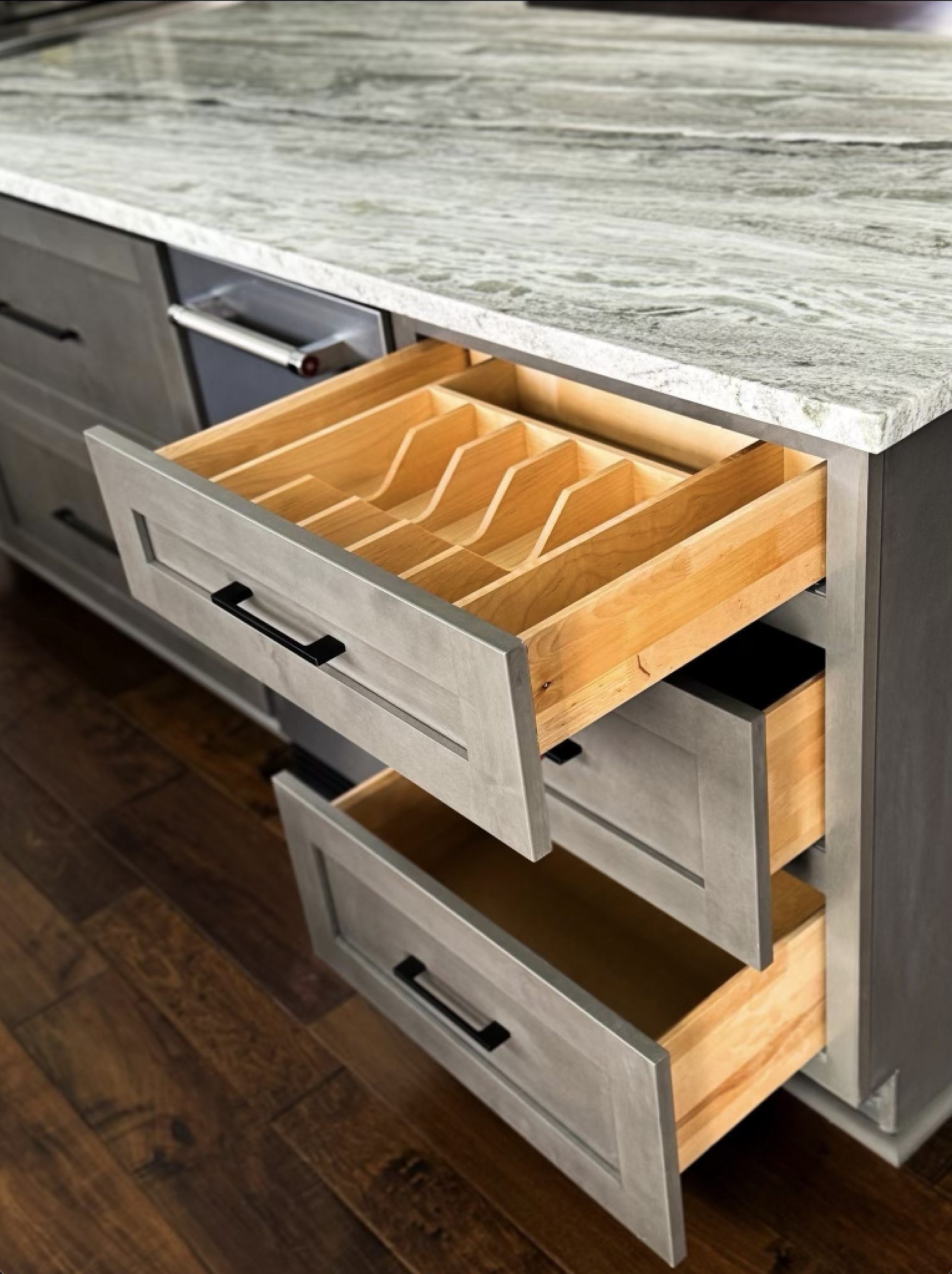 Open kitchen drawers with wooden dividers and a marble countertop.
