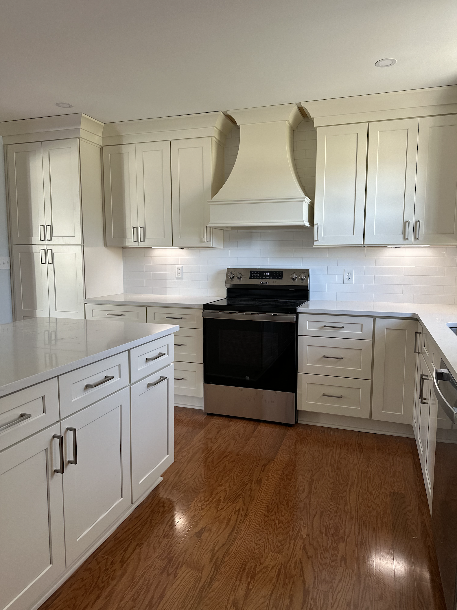 Modern kitchen with white cabinets, a white subway tile backsplash, a black and stainless steel oven, and hardwood floors.