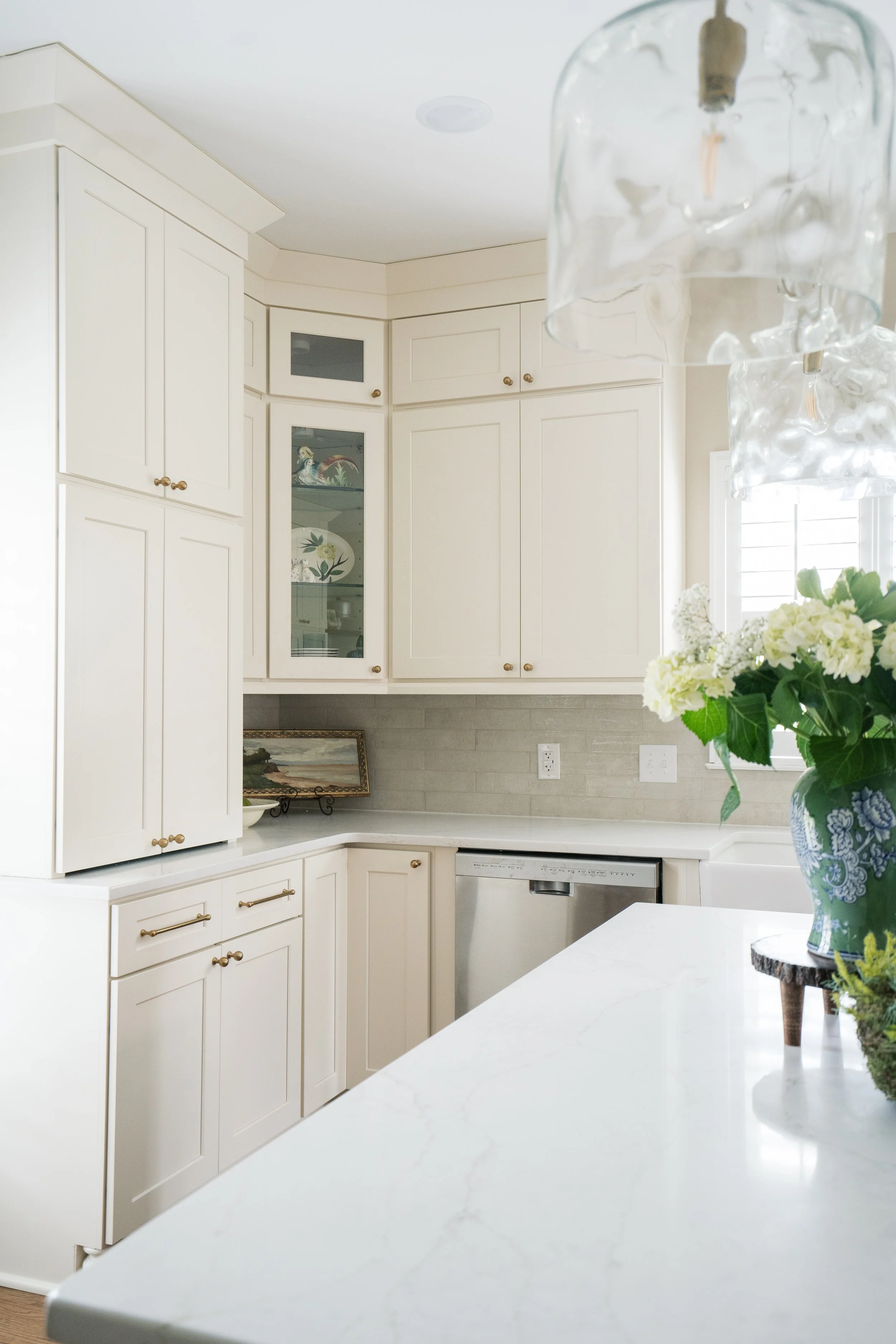Bright kitchen with white cabinets, a marble countertop, a window with shutters, and a blue and white vase with flowers.