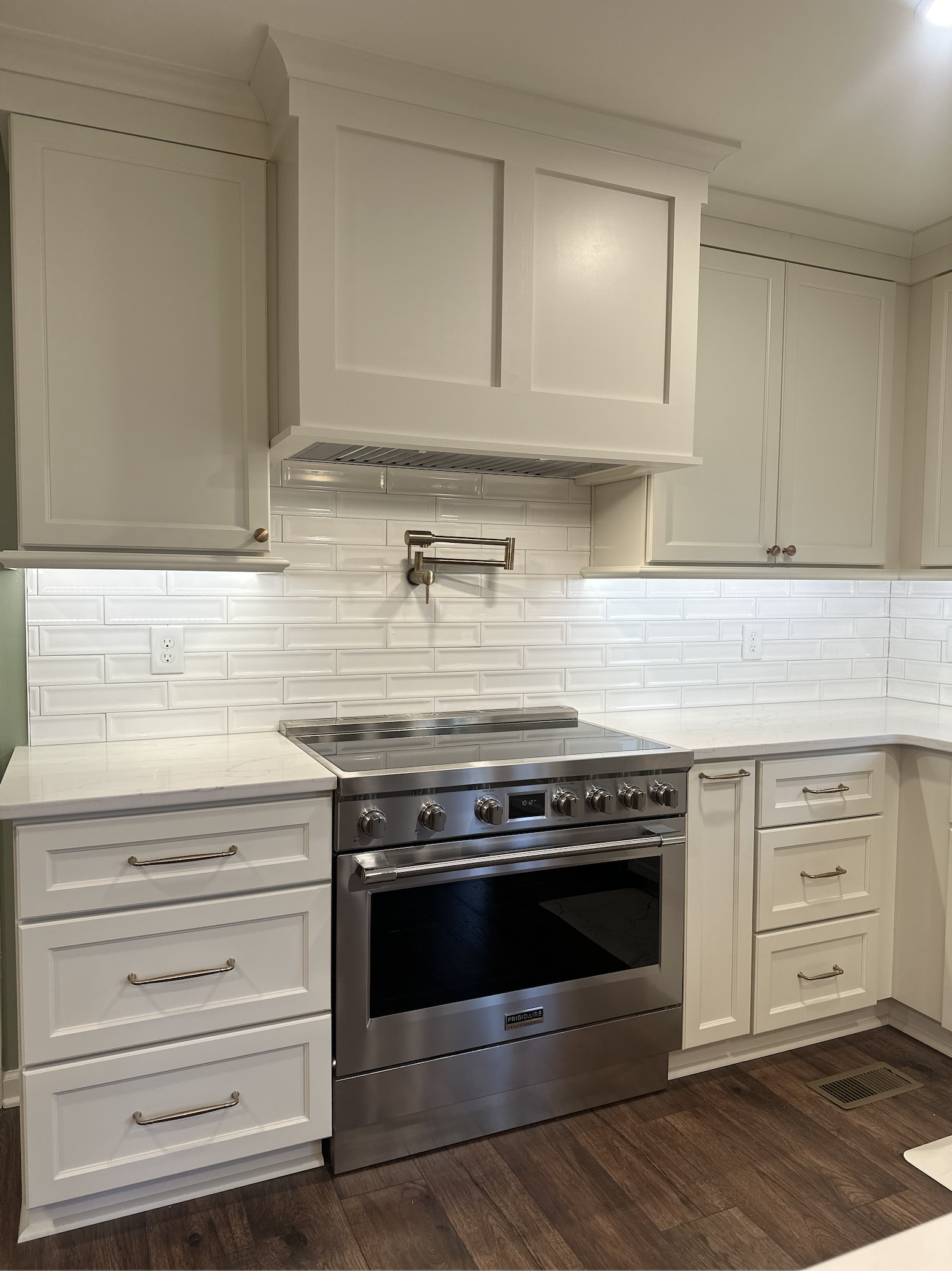White kitchen with white cabinets, a stainless steel stove, a white countertop, and a white subway tile backsplash with a wall-mounted pot filler faucet.