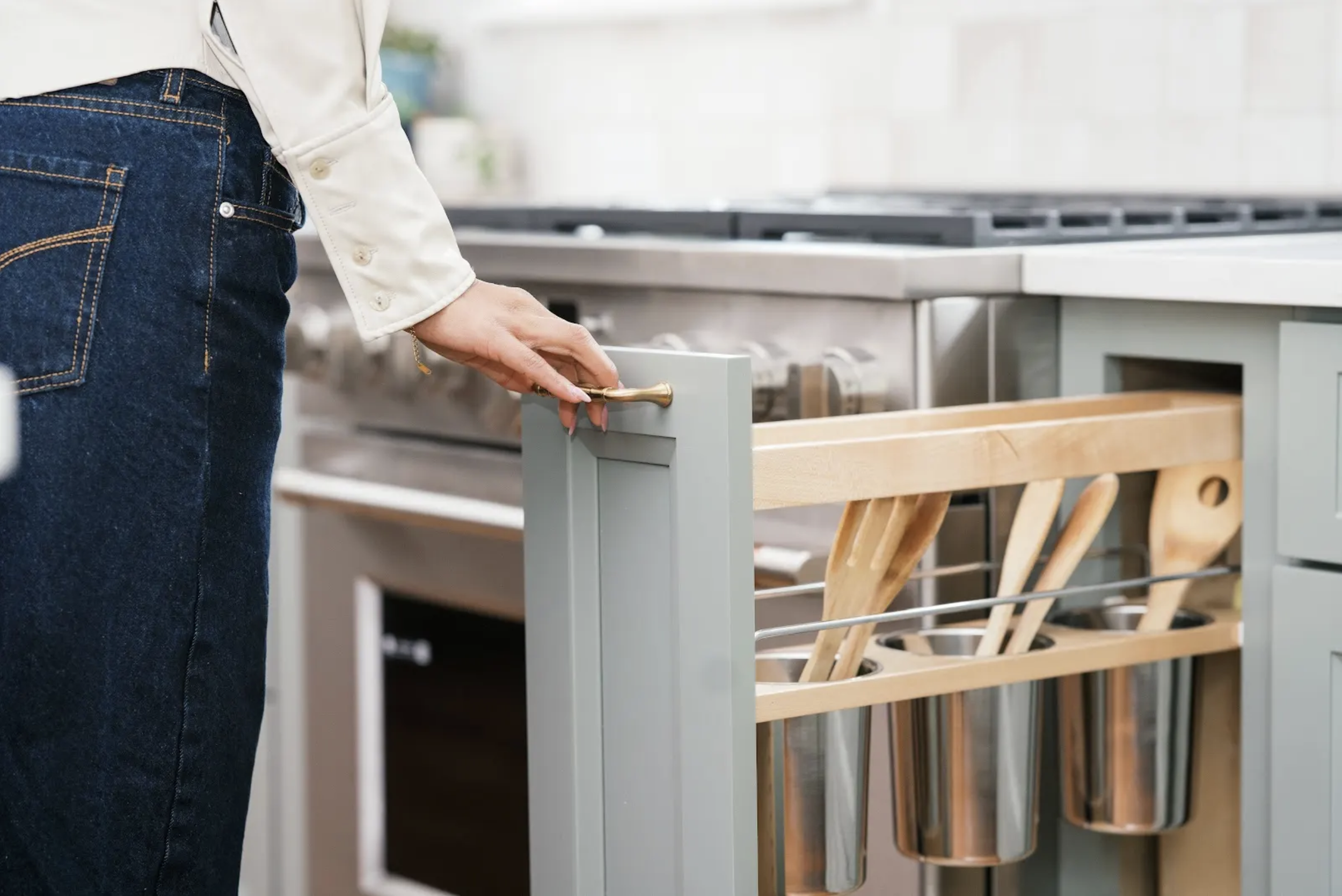 Person opening a kitchen drawer with wooden utensils and metallic cups inside.