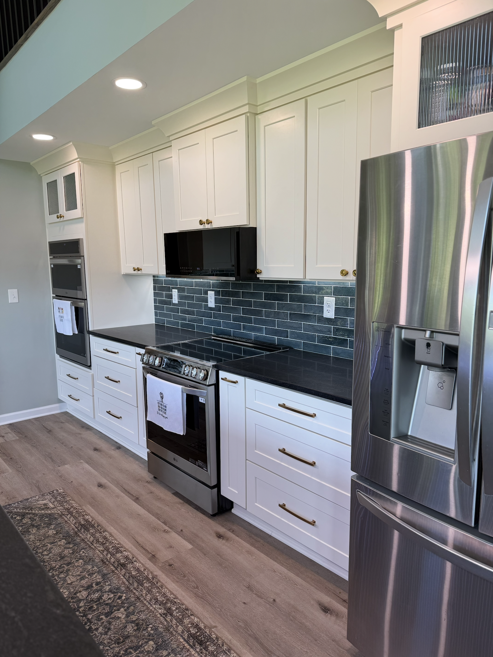 Modern kitchen with white cabinets, black countertops, a black backsplash, stainless steel appliances including a refrigerator, oven, microwave, and electric stove, with a wooden floor.