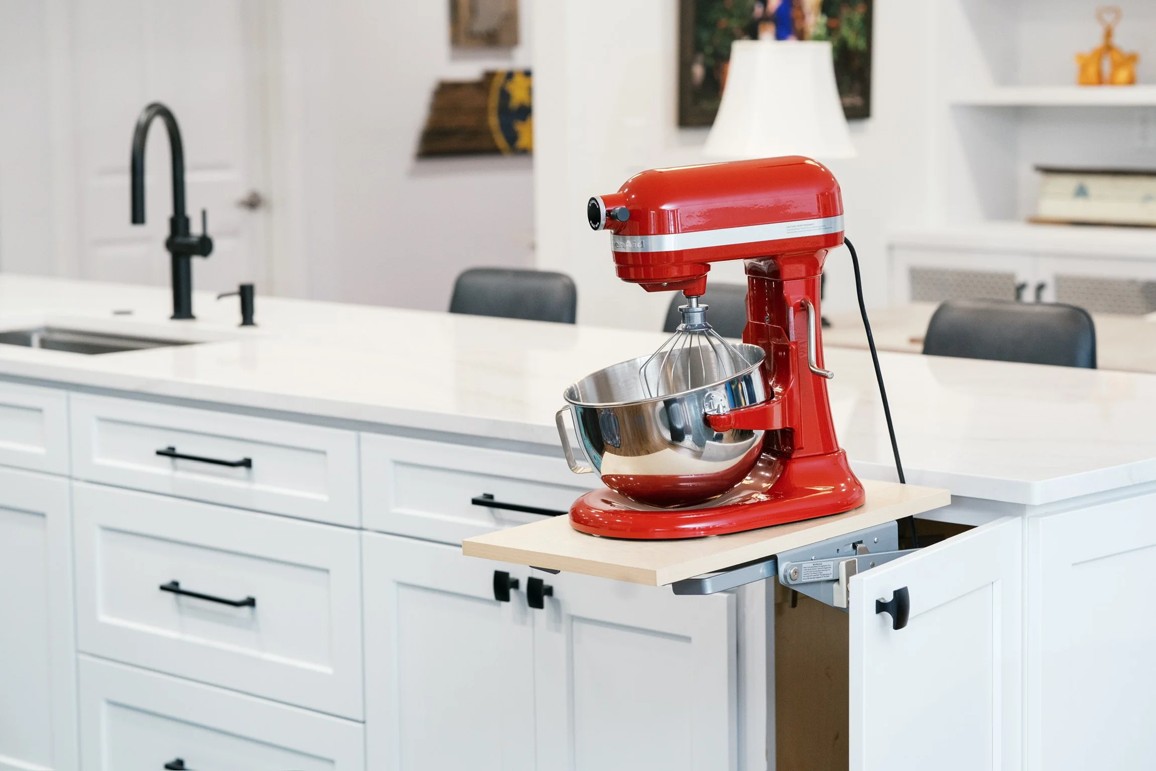 A red stand mixer with a stainless steel mixing bowl on a kitchen countertop, with a pull-out extension for additional workspace.