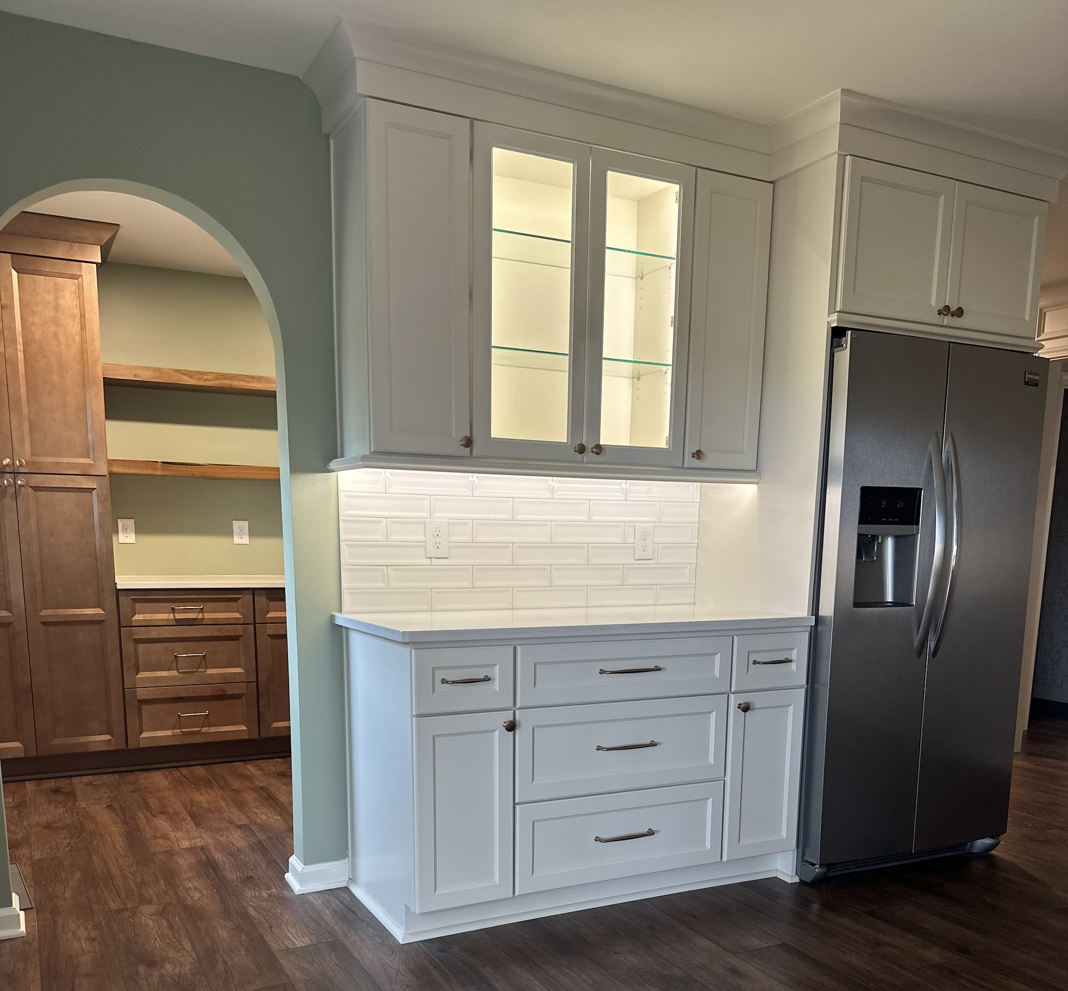 Kitchen with white cabinets, a glass-front upper cabinet, a stainless steel side-by-side refrigerator, and a white subway tile backsplash.